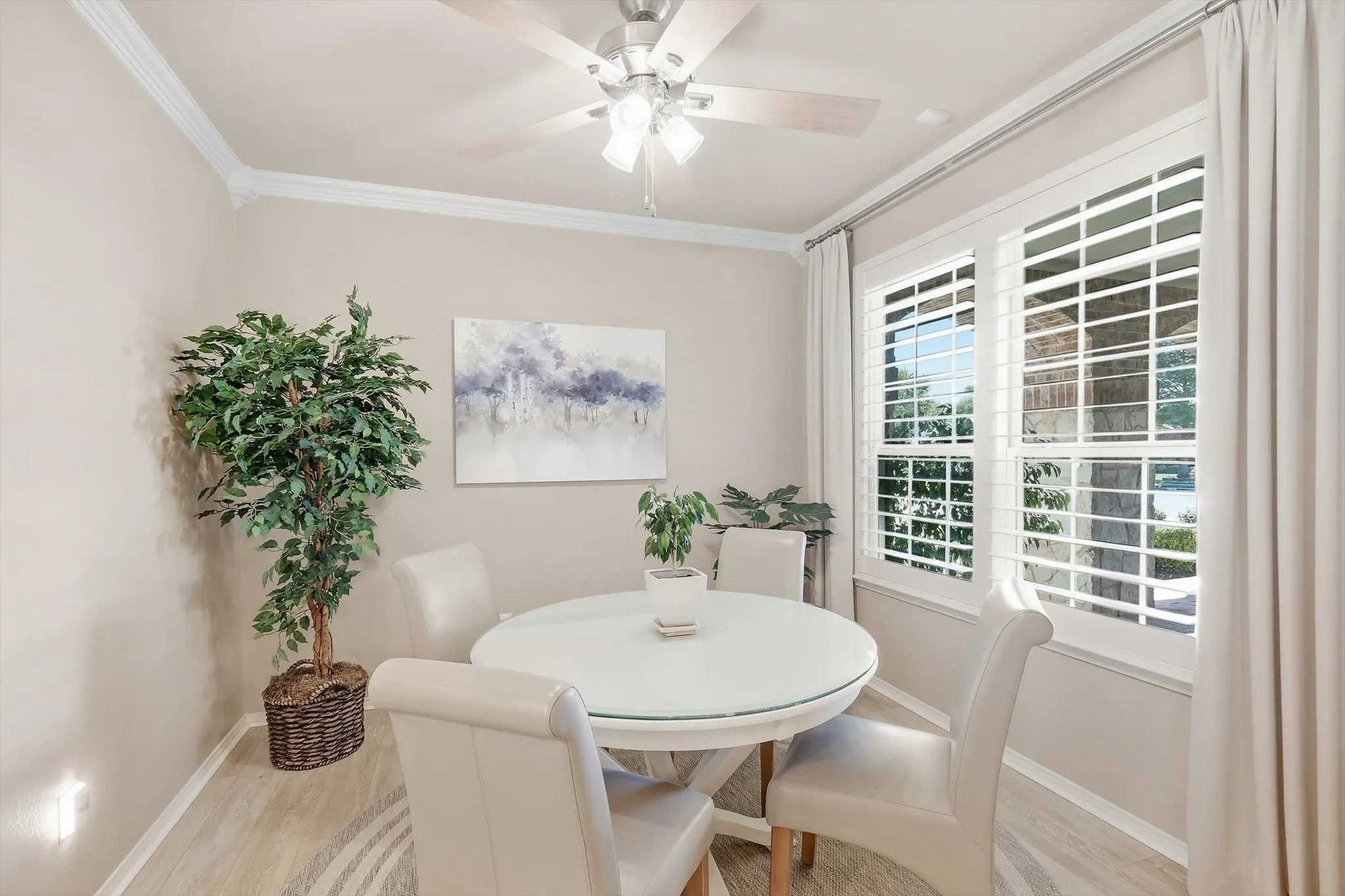 Crown molding accenting the ceiling, wood-finish flooring, two large windows with plantation shutters, ceiling fan with integrated lighting, and neutral wall tones