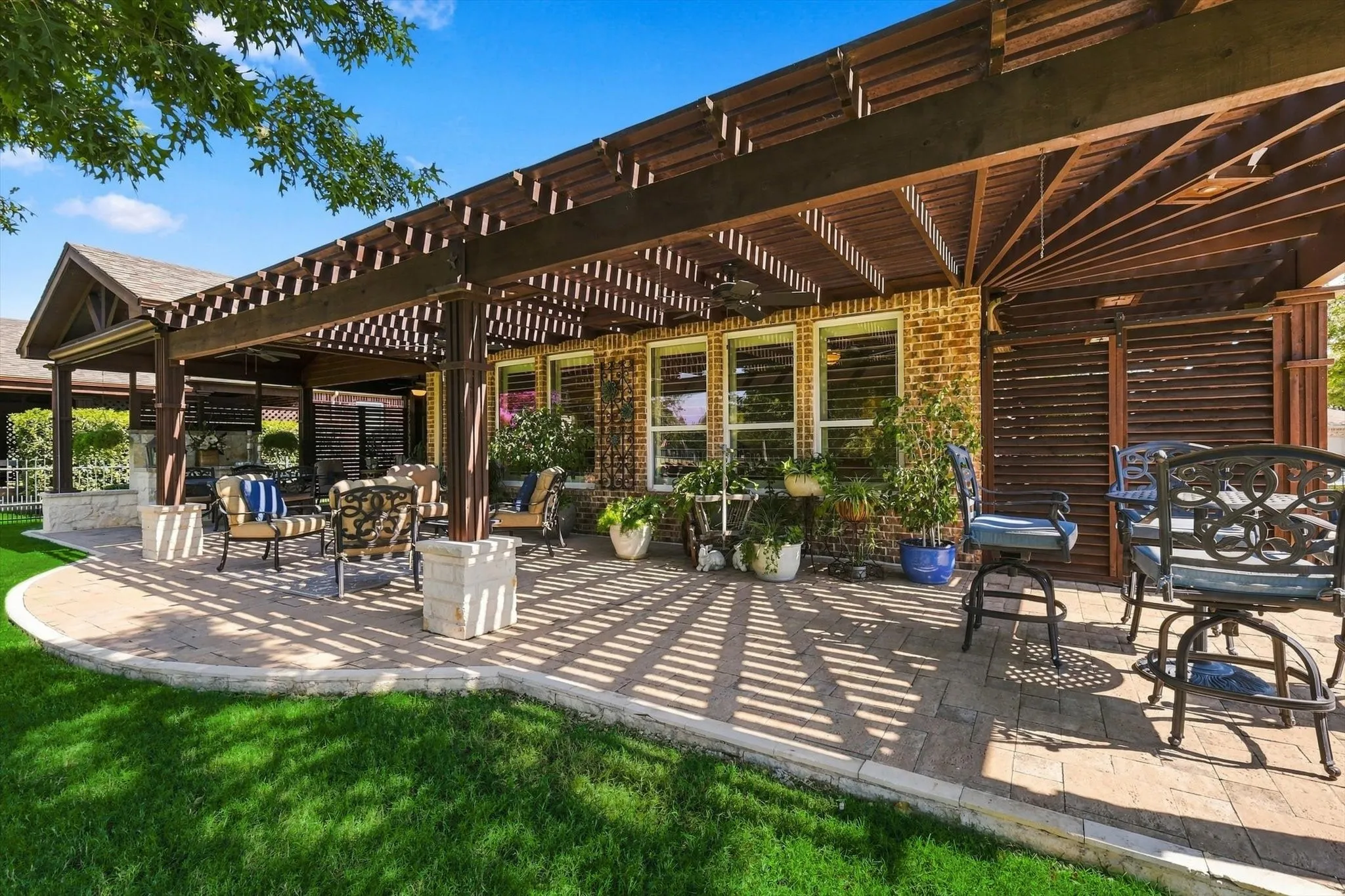 Expansive paver patio with a wood pergola, brick exterior, and multiple windows