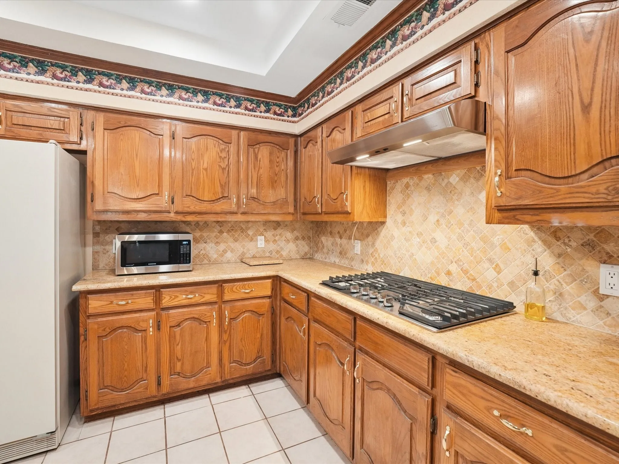 Recessed ceiling with an overhead light fixture, wood-finish cabinetry, tile flooring, and a built-in gas cooktop
