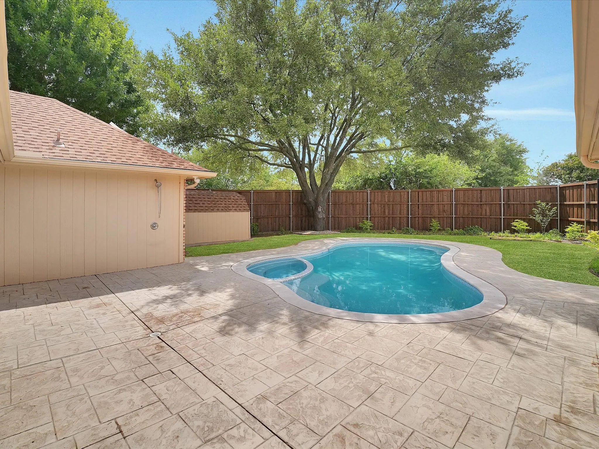 Resort-style backyard featuring a free-form swimming pool with integrated spa, stamped concrete patio, and a privacy fence