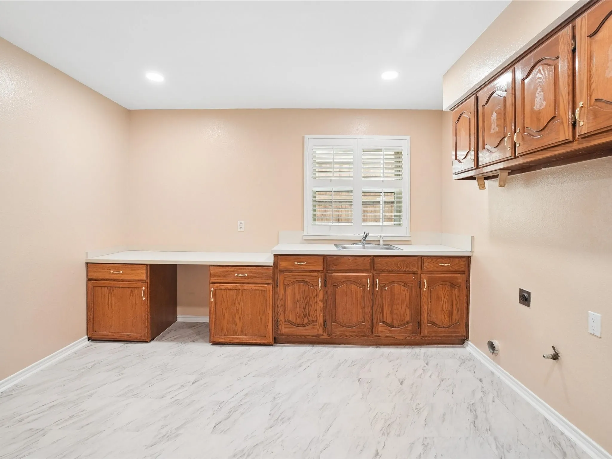 Functional utility room featuring wood-finish cabinetry, white countertops, and a stainless steel sink
