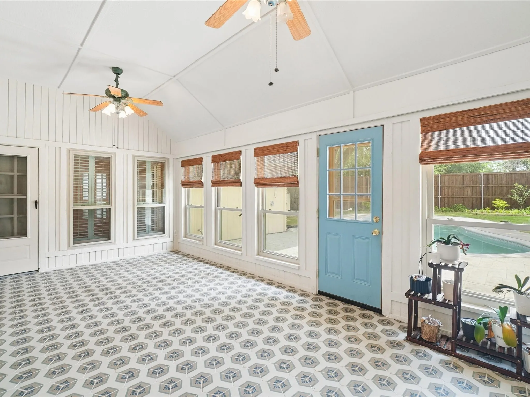 Vaulted ceiling with exposed beams, decorative ceiling fans, patterned tile flooring, multiple windows with blinds, and an exterior door with glass panels