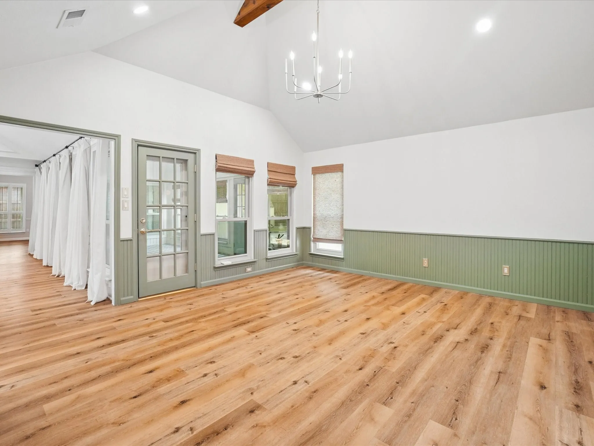 Vaulted ceiling with an exposed wood beam, wood-finish flooring, two large windows, a glass-paned door, and beadboard wainscoting