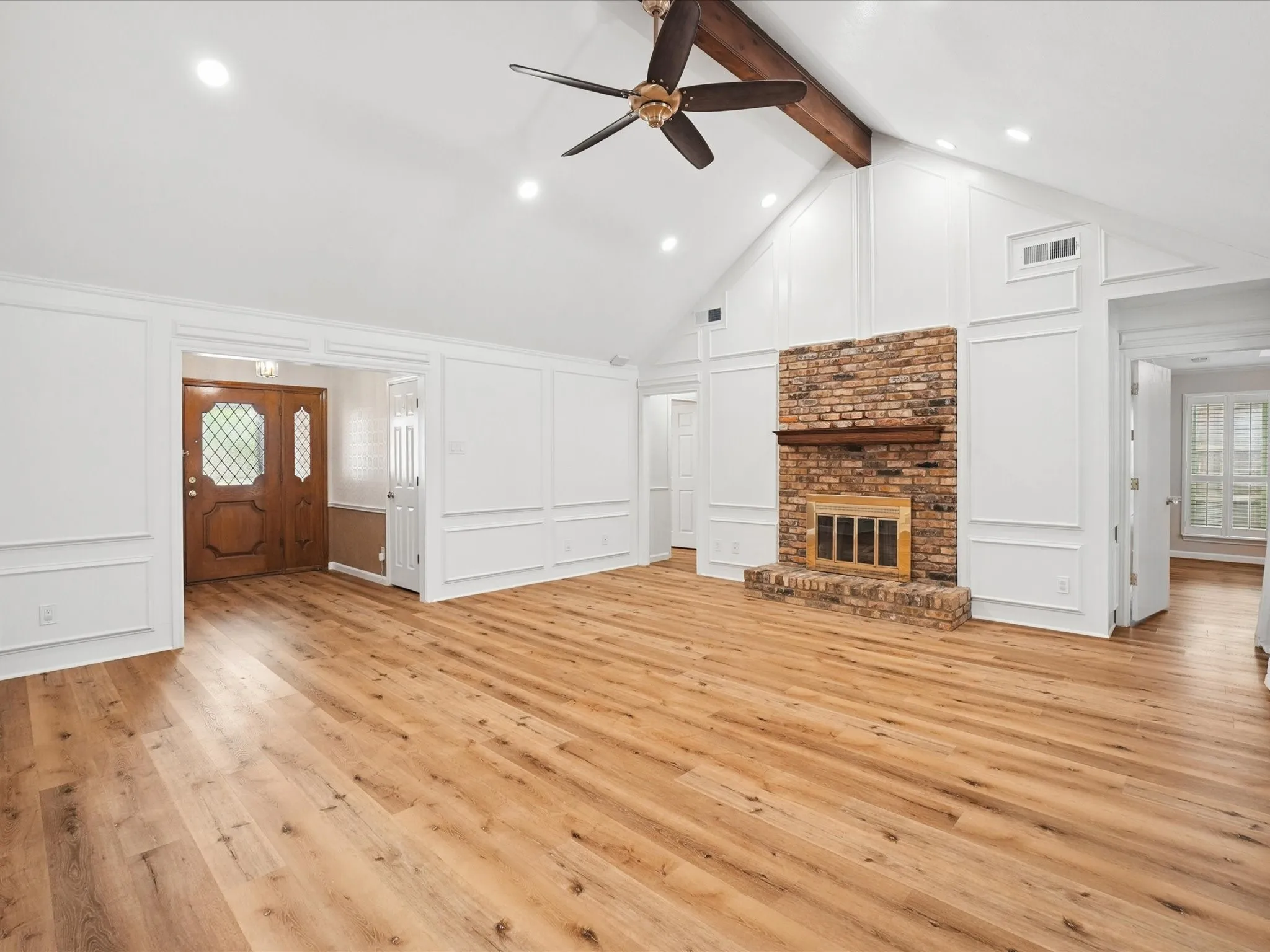 Vaulted ceiling with exposed wood beam, recessed lighting, wood-finish flooring, brick fireplace with mantel, and decorative wall paneling
