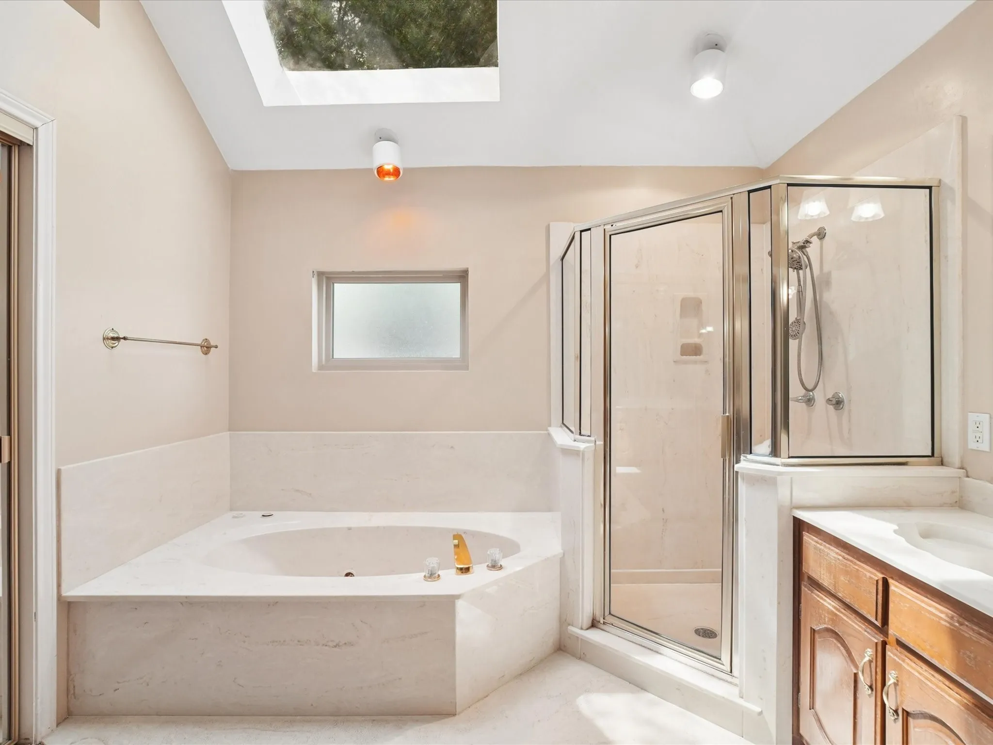Recessed corner tub with integrated jets, glass-enclosed shower, wood vanity with integrated sink, and overhead skylight