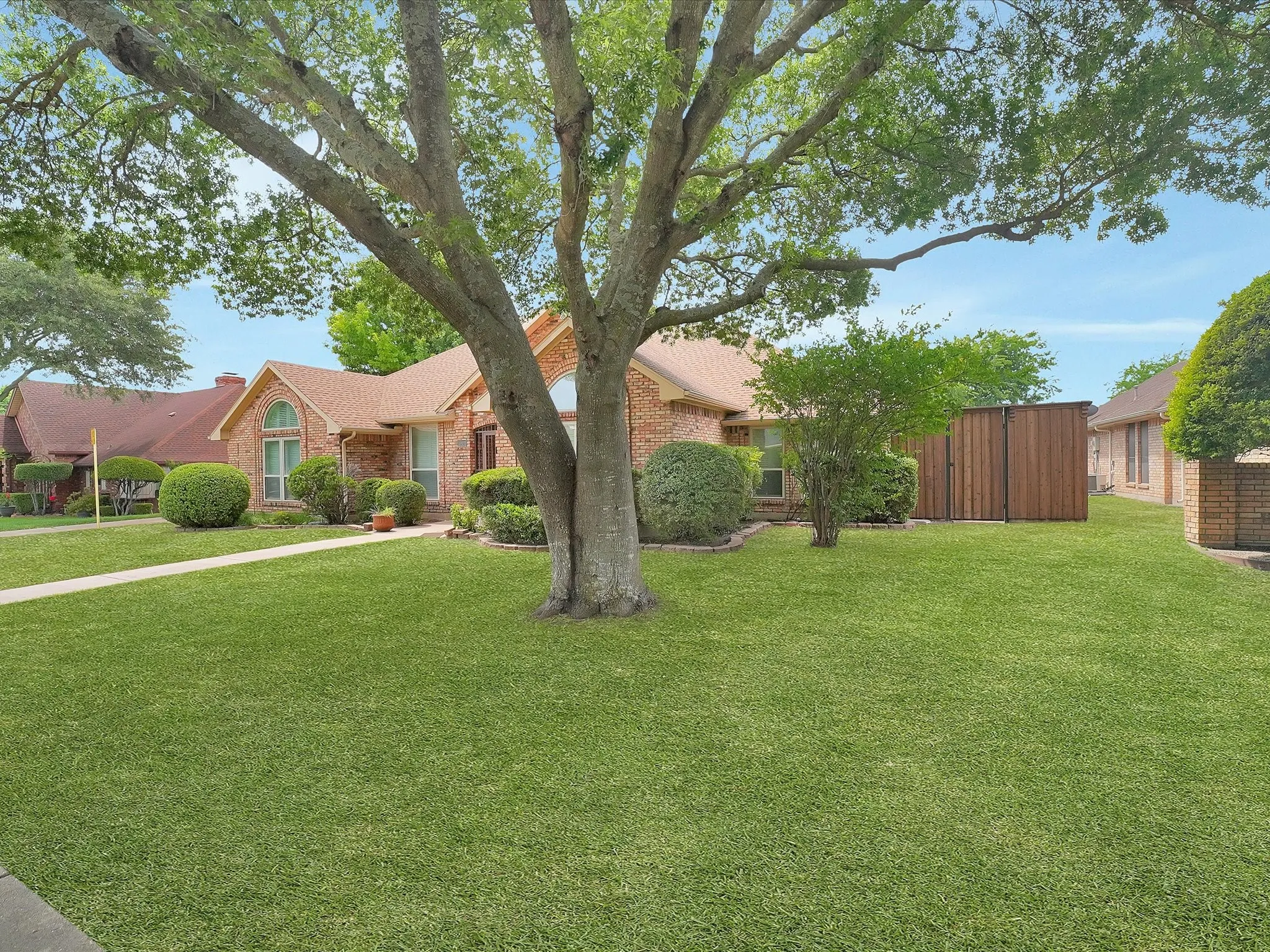 Brick exterior, gabled roof, arched window, mature tree, manicured lawn