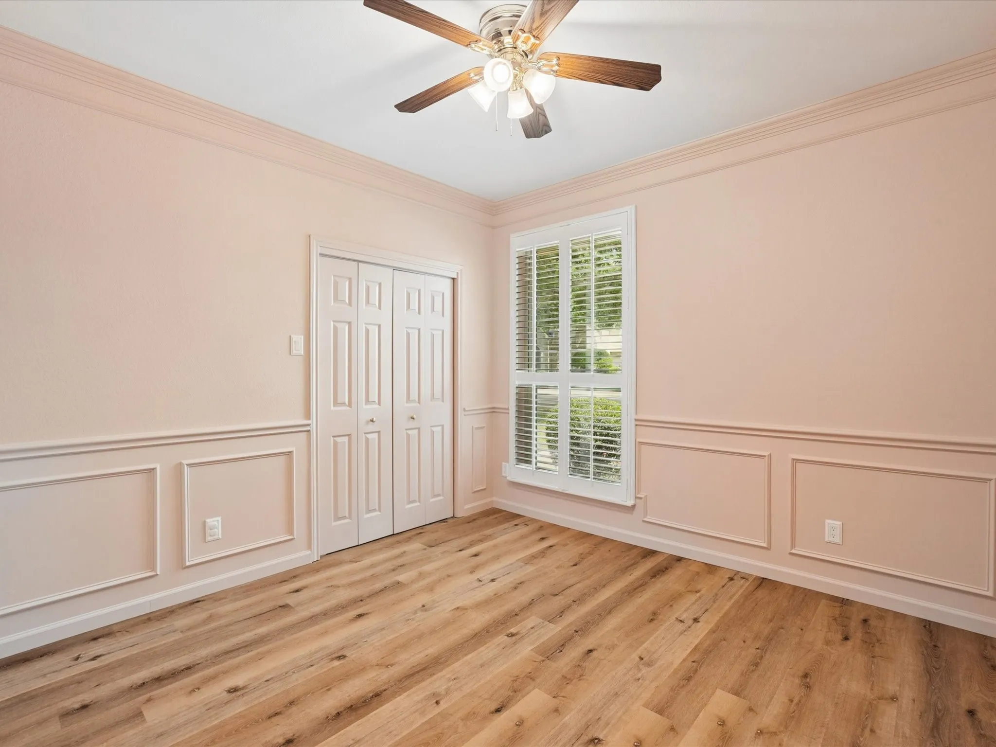 Wood-finish flooring, crown molding, wainscoting, bi-fold closet doors, and a ceiling fan with light fixture