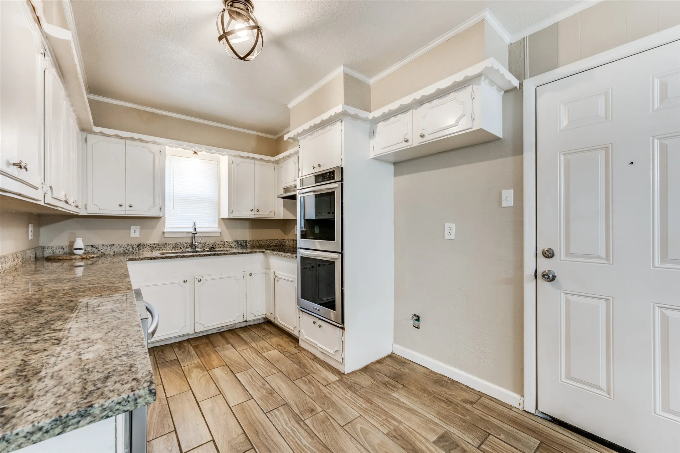 Kitchen with white cabinetry, wood-finish flooring, light-toned countertops, and built-in double ovens
