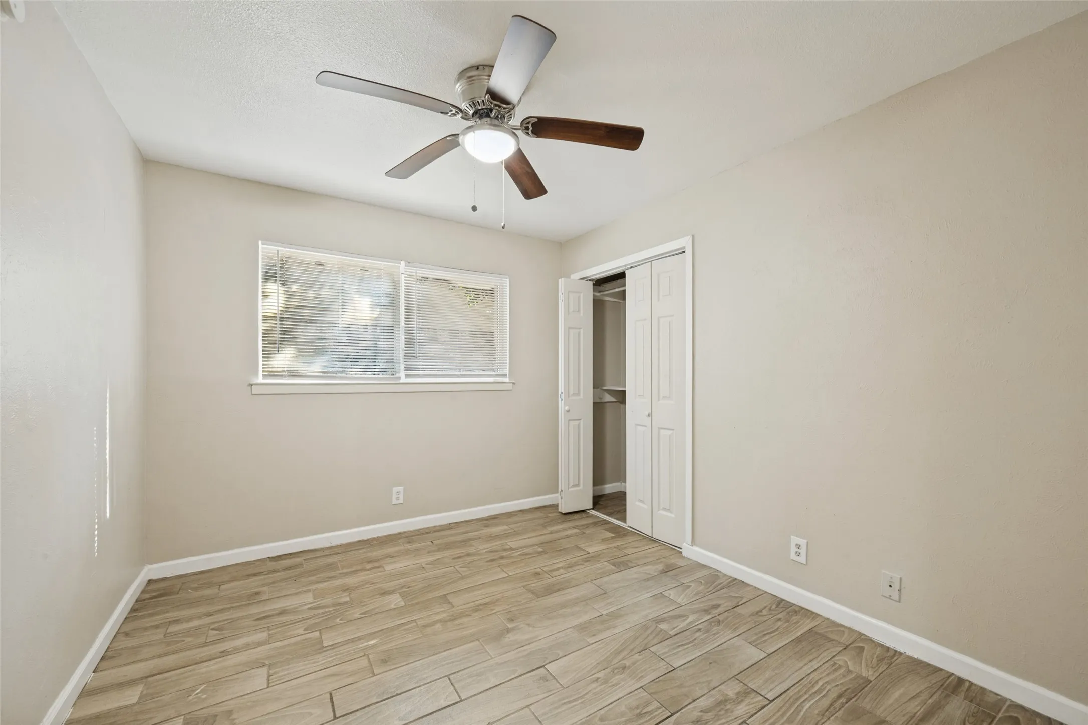 Wood-finish tile flooring, ceiling fan with integrated lighting, and a window with blinds