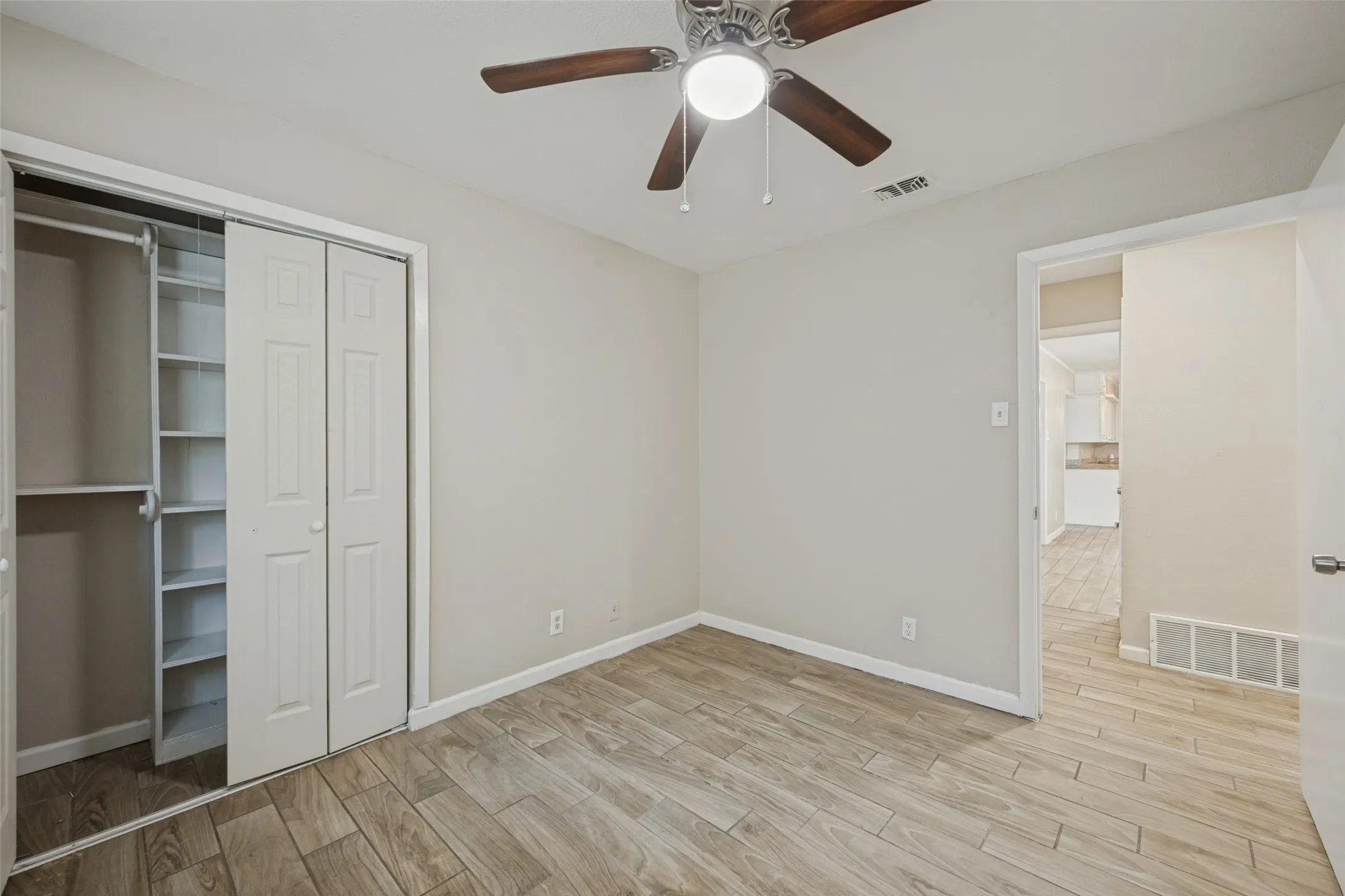 Wood-finish flooring throughout, ceiling fan with integrated lighting, bi-fold closet doors, and built-in shelving