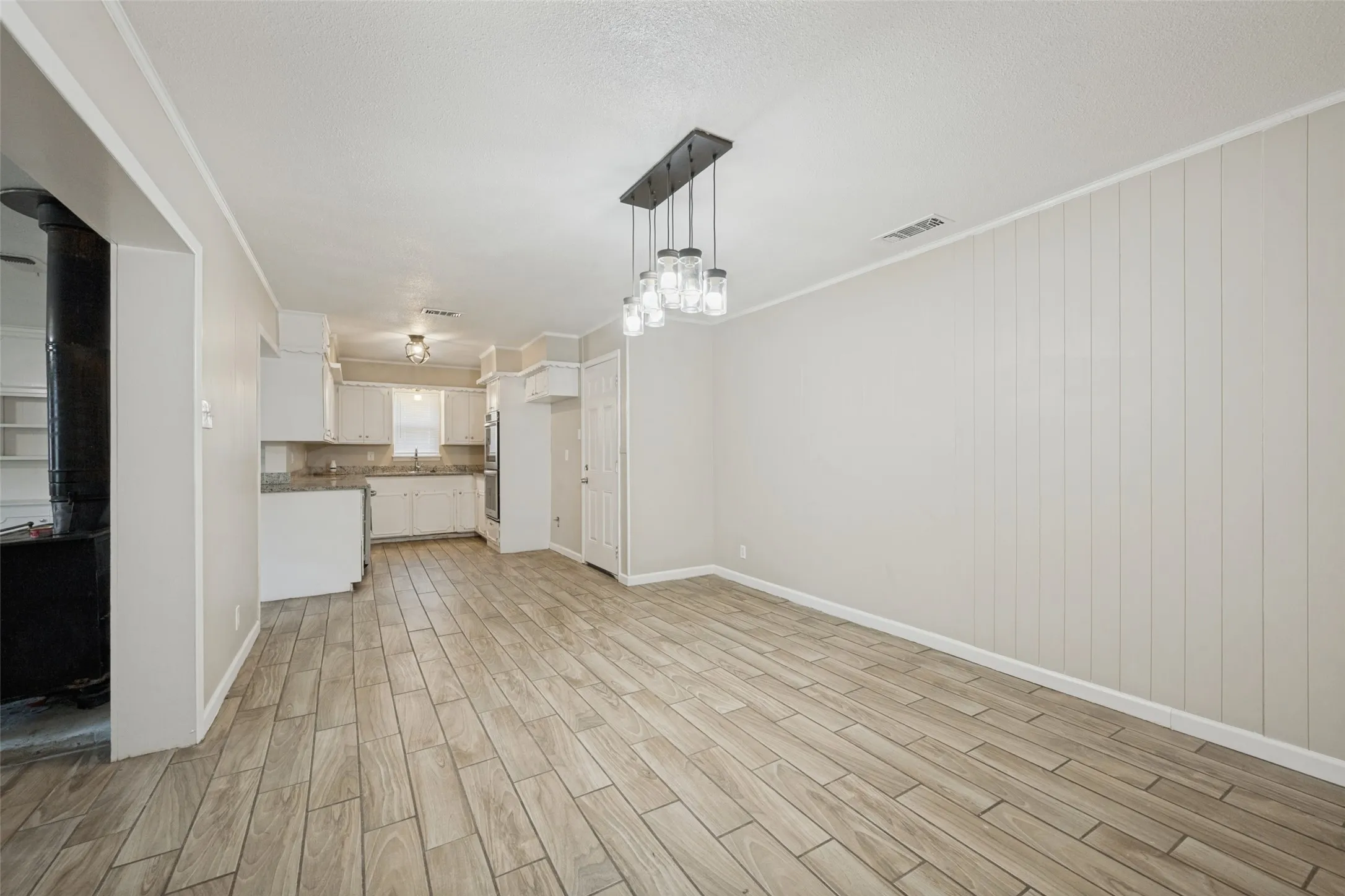 Open-concept living area featuring wood-look tile flooring, a multi-light chandelier, and panel accent wall