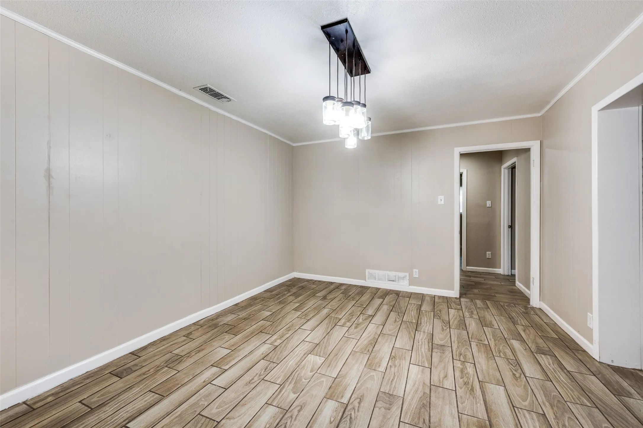 Neutral wall paneling, wood-finish flooring, and a modern linear chandelier with glass shades