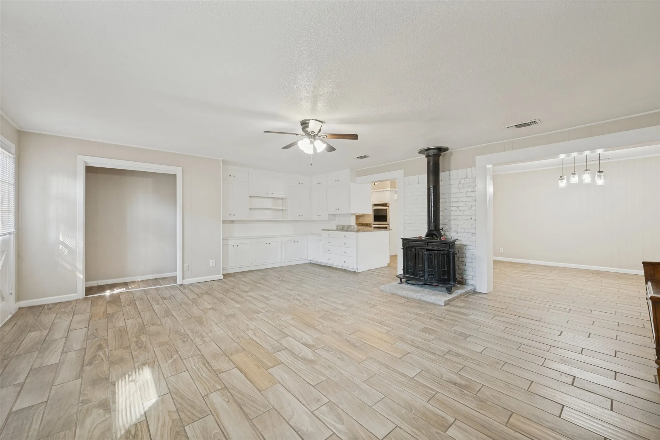 Wood-finish tile flooring throughout, white cabinetry with built-in shelving, stove-style fireplace with white brick surround, and a ceiling fan