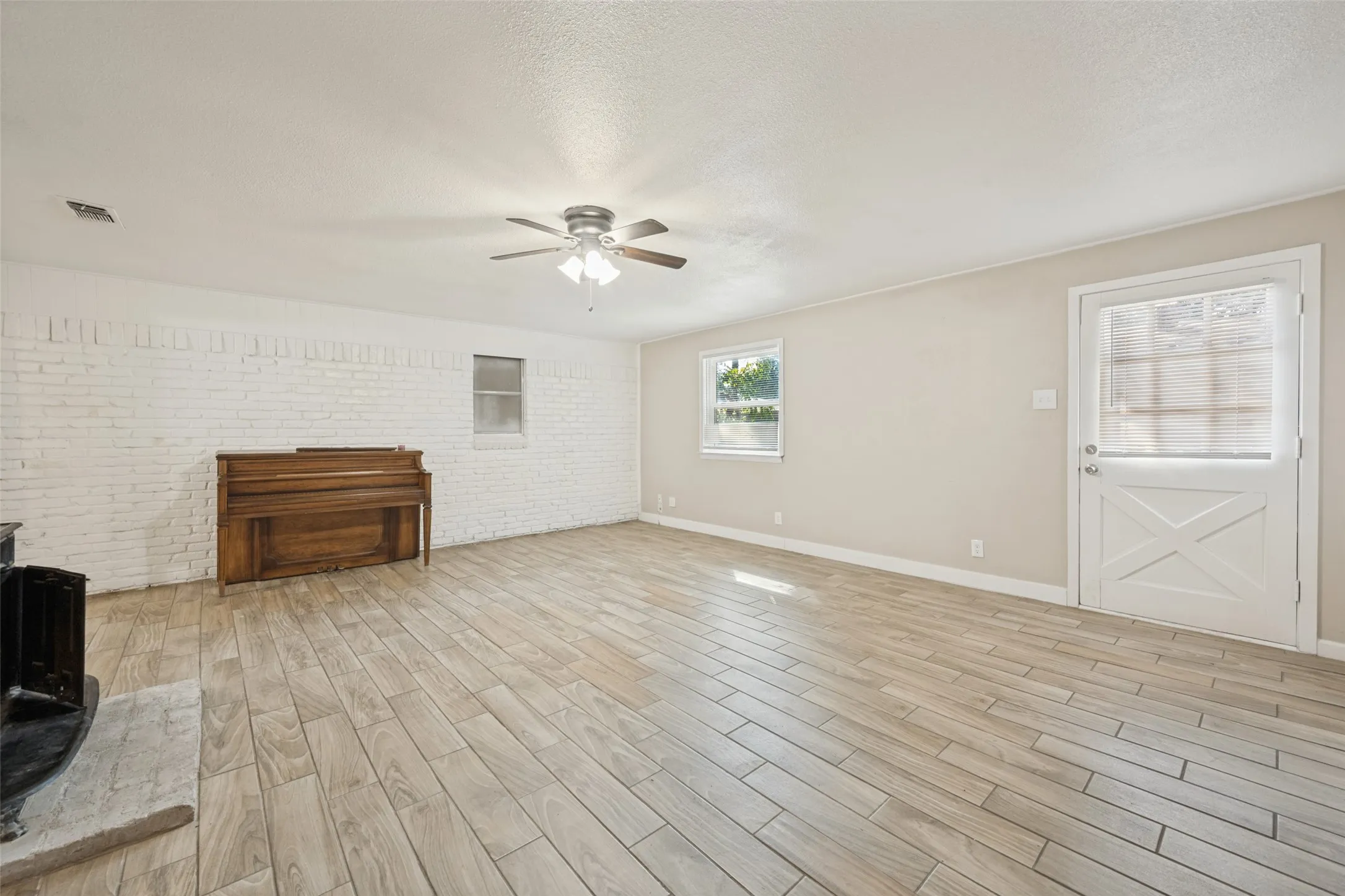 Wood-finish flooring, white painted brick accent wall, ceiling fan, and a Dutch door with opaque glass panels