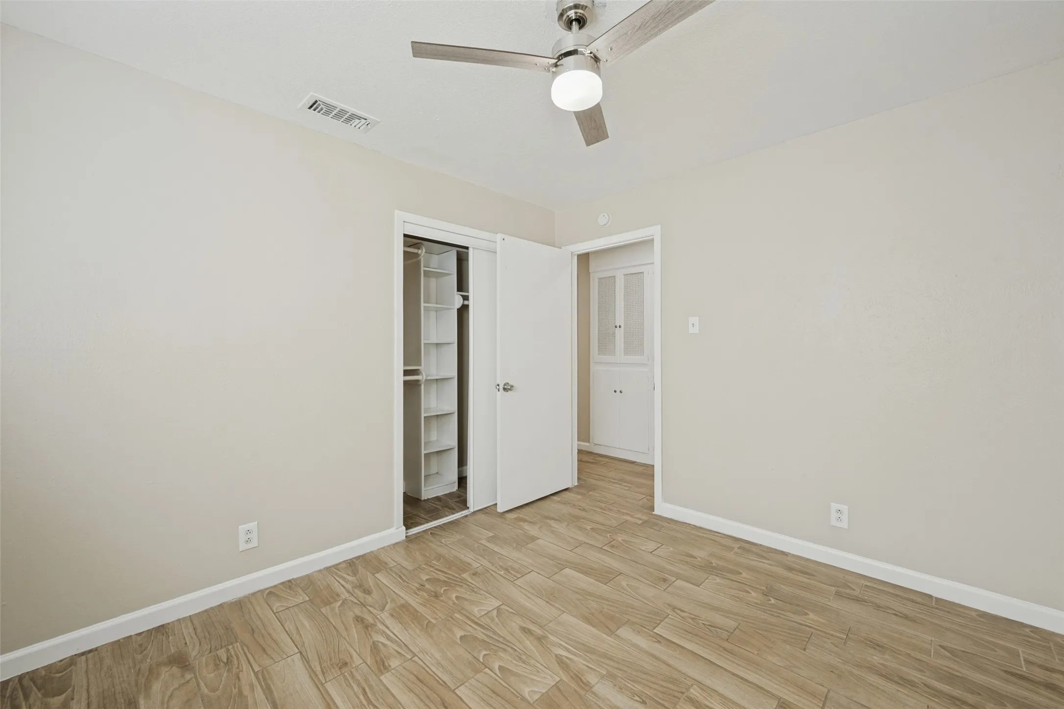 Wood-finish flooring, ceiling fan with integrated lighting, and a built-in closet system