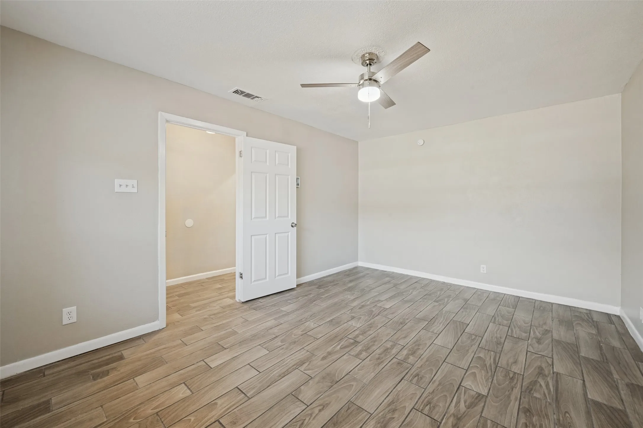 Wood-finish tile flooring throughout, neutral paint palette, and a ceiling fan with integrated lighting