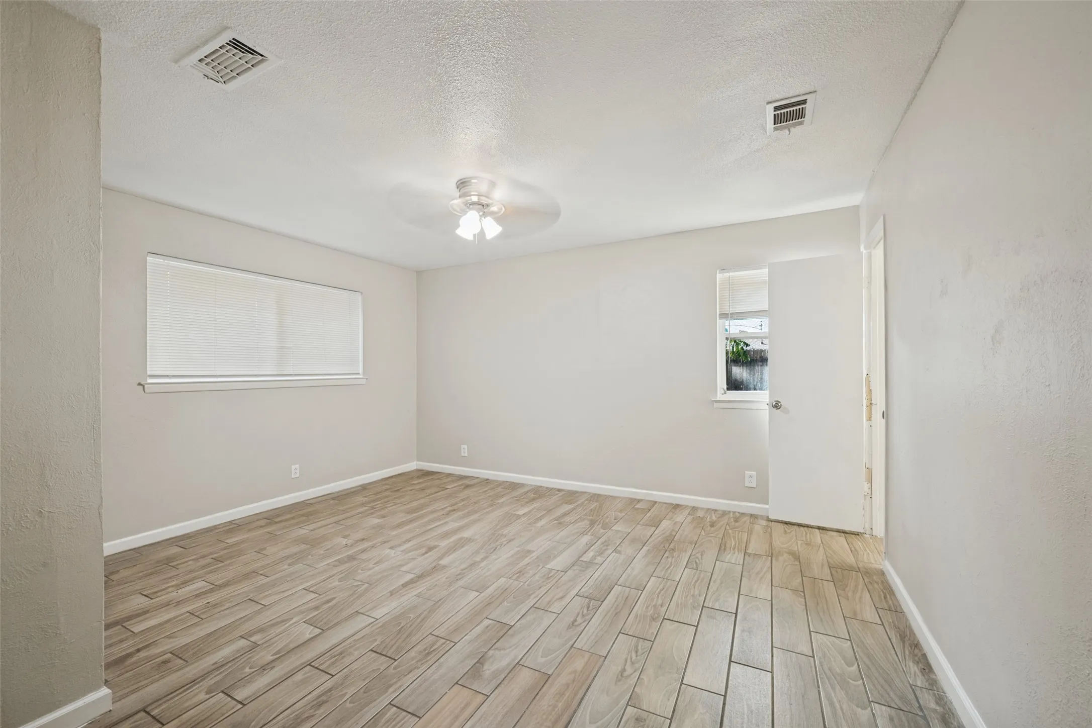 Spacious room featuring wood-finish tile flooring, neutral wall tones, window blinds, and a ceiling fan with integrated lighting