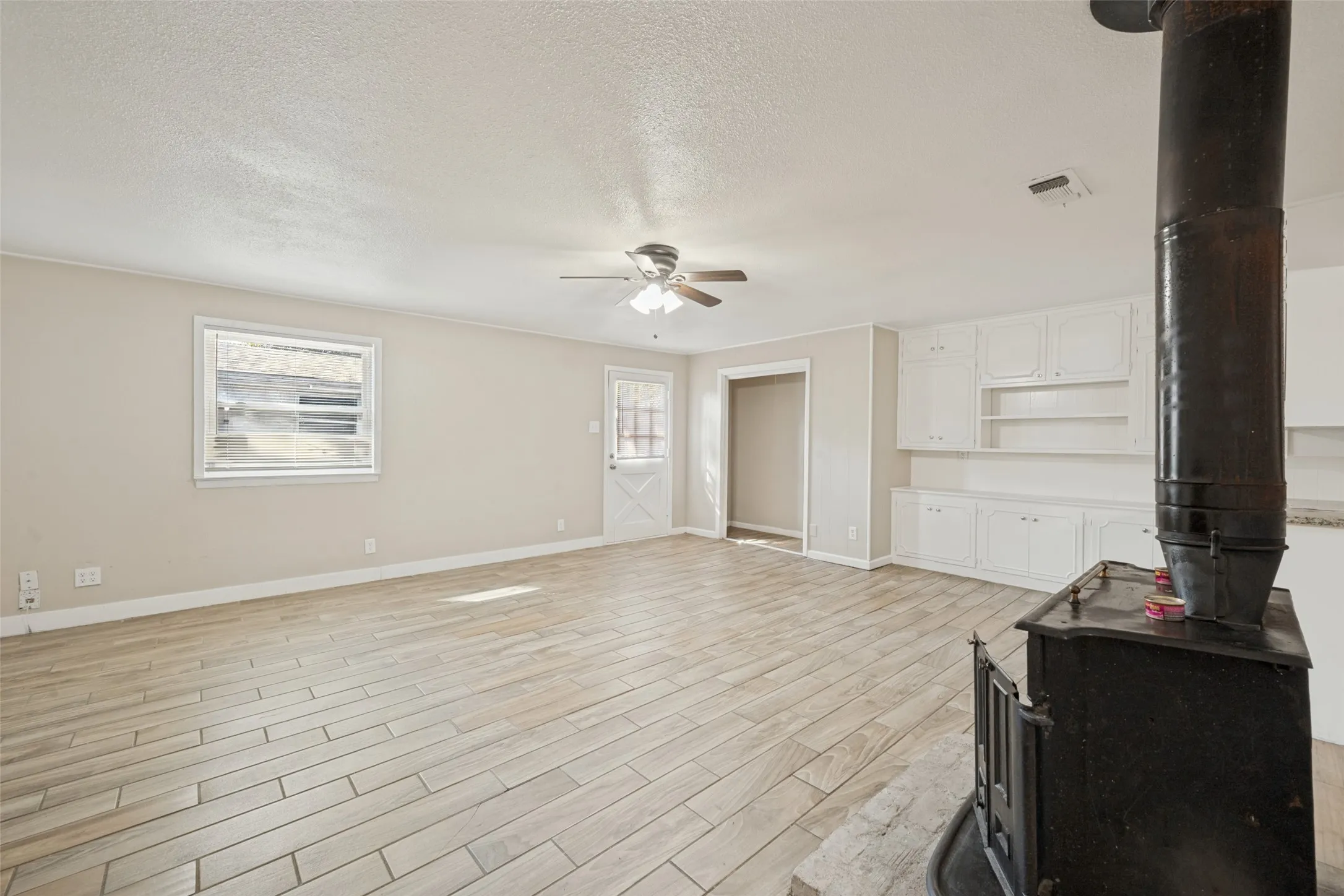 Spacious living area featuring wood-finish tile flooring, a built-in wood-burning stove, white built-in cabinetry, and a ceiling fan