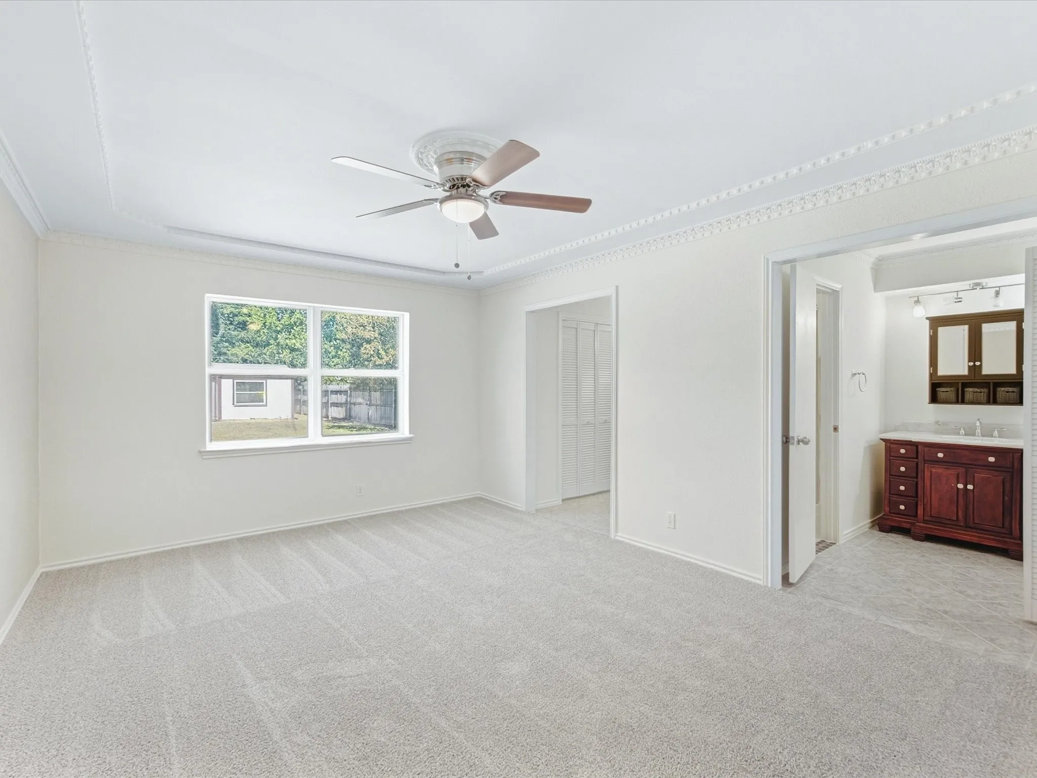 Spacious Primary Bedroom with light gray carpet, a ceiling fan with light kit, and decorative crown molding