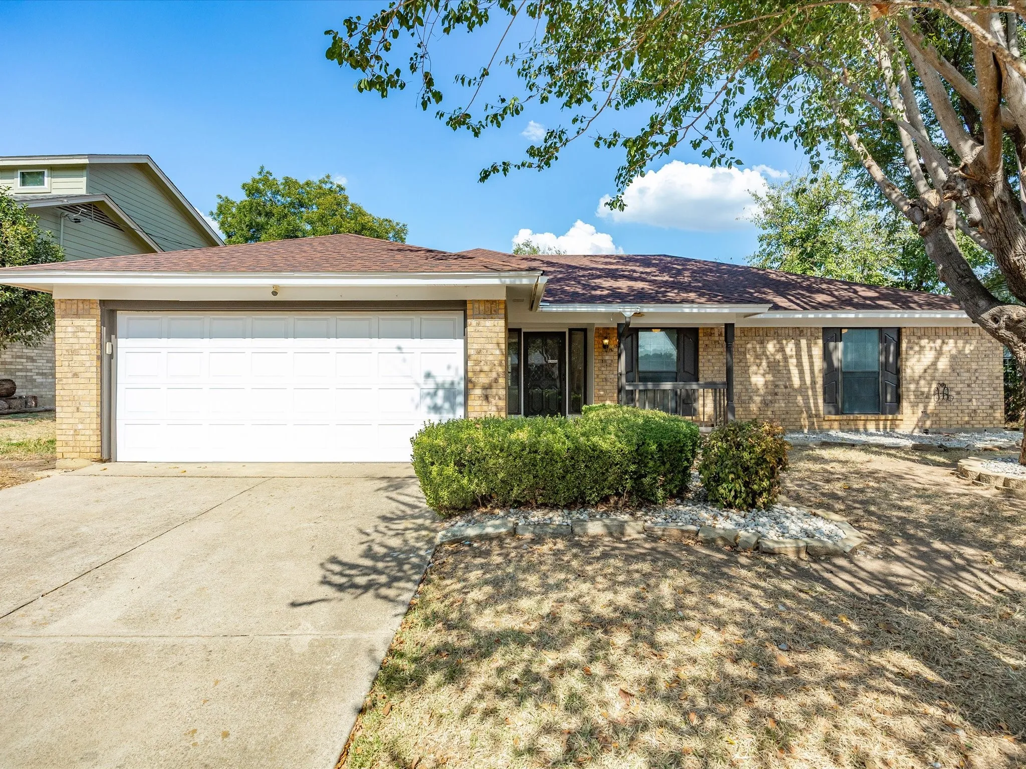 Brick exterior with an attached garage, covered entry, and established landscaping