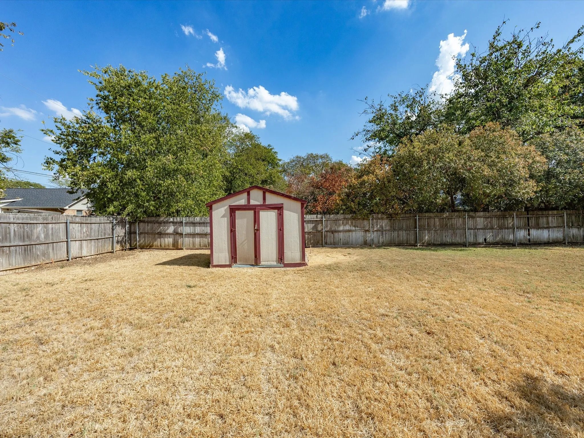 Fully fenced backyard featuring a storage shed and mature trees