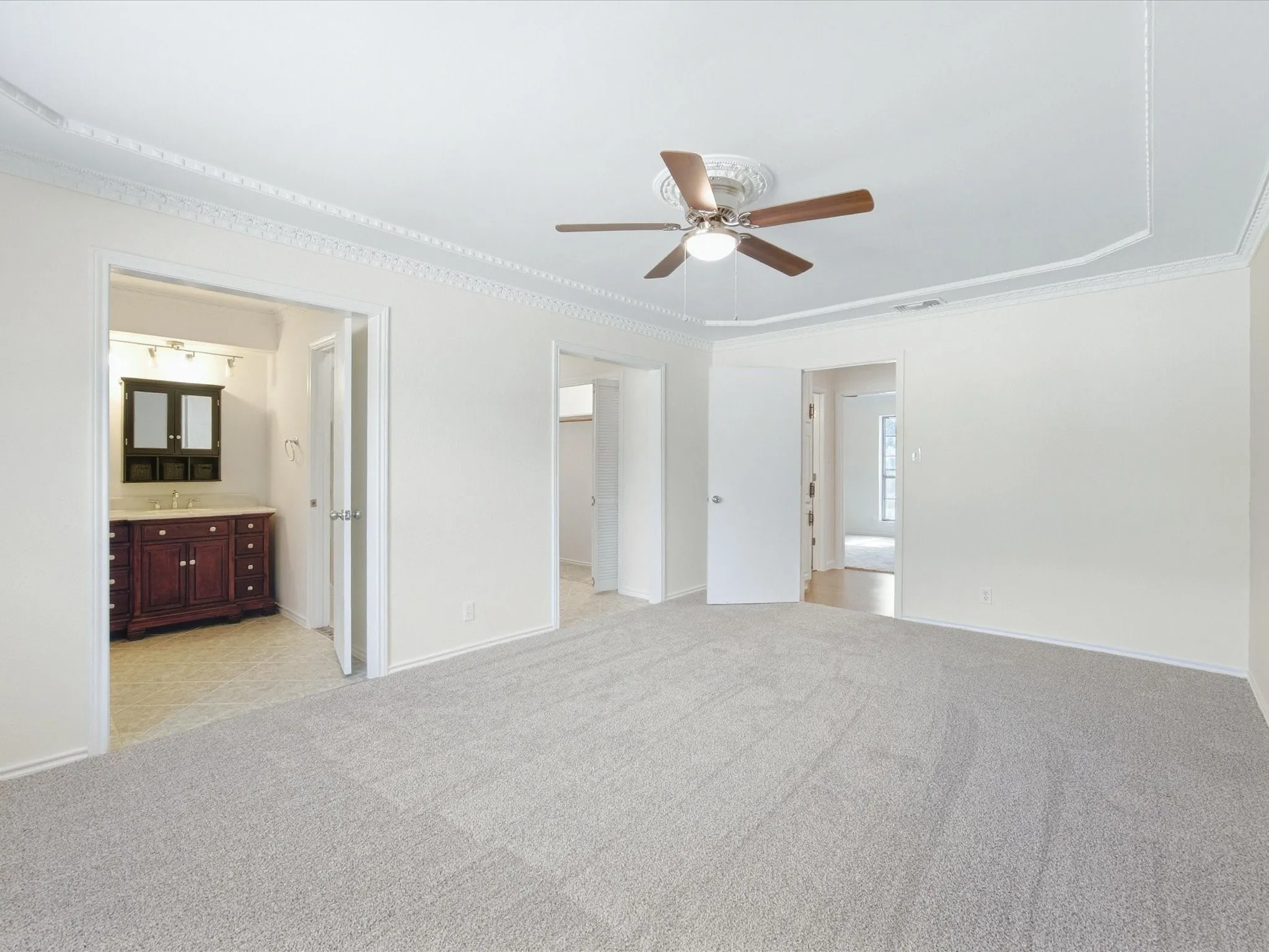 Tray ceiling with decorative crown molding, ceiling fan, and light gray carpeted flooring