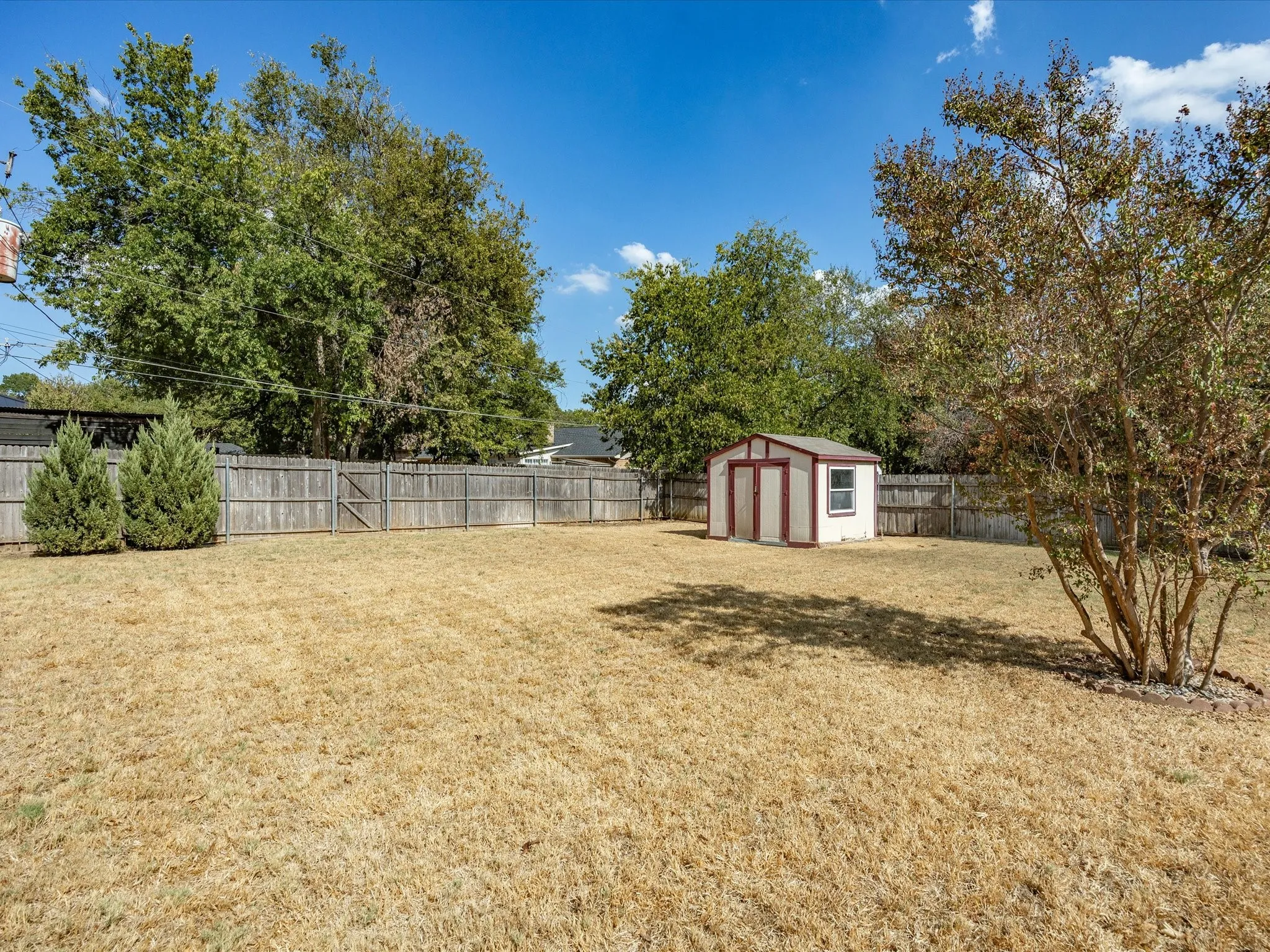 Fenced yard with a storage shed, established trees, and shrubbery