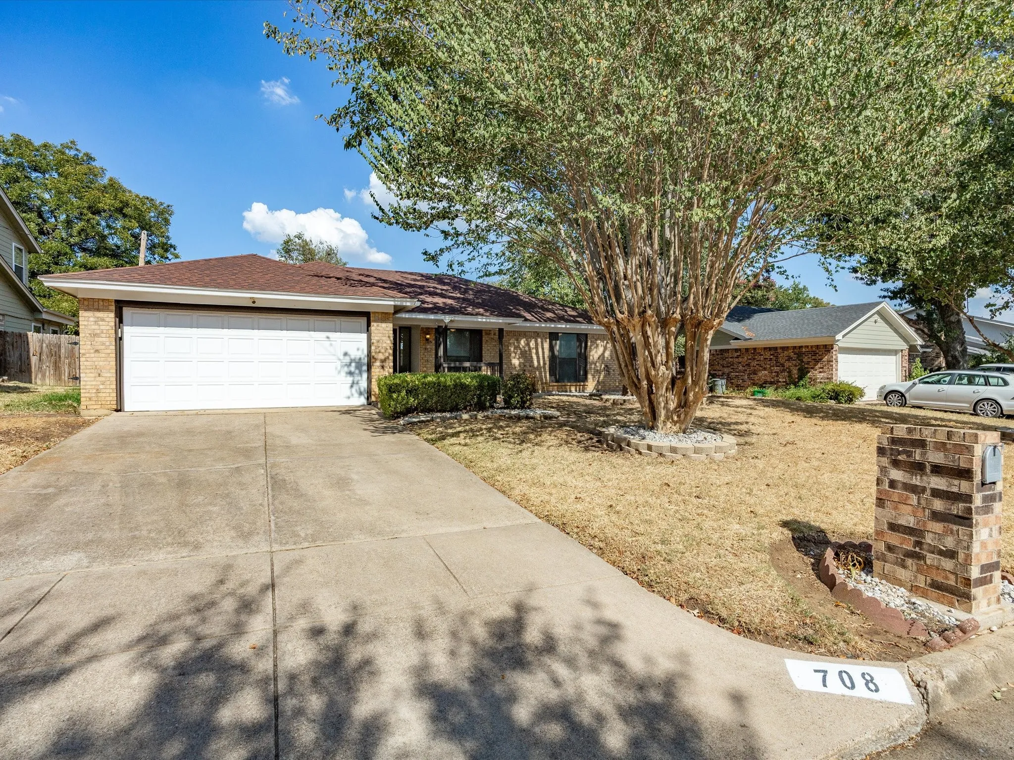 Brick-clad exterior with a two-car garage, concrete driveway, and mature tree