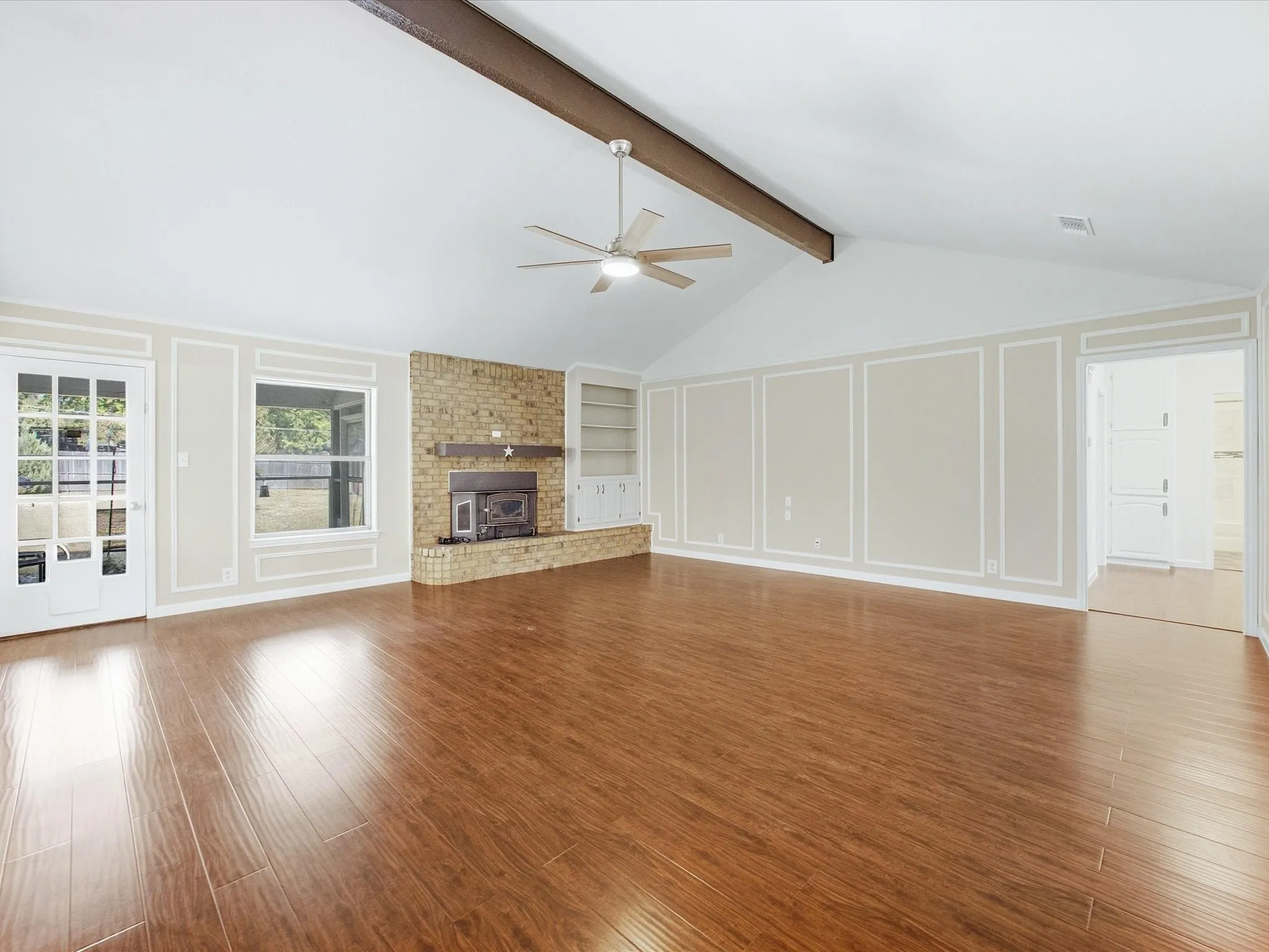 Vaulted ceiling with exposed beam, wood-finish flooring, brick fireplace, built-in shelving, and panel molding