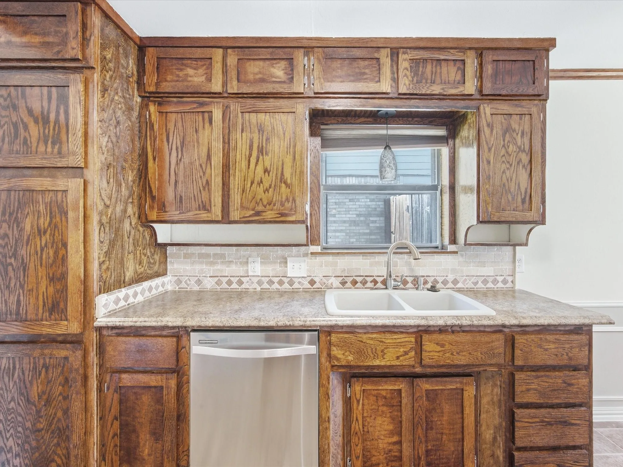 Wood cabinetry, dual basin sink, stainless steel dishwasher, tile backsplash, and composite countertop