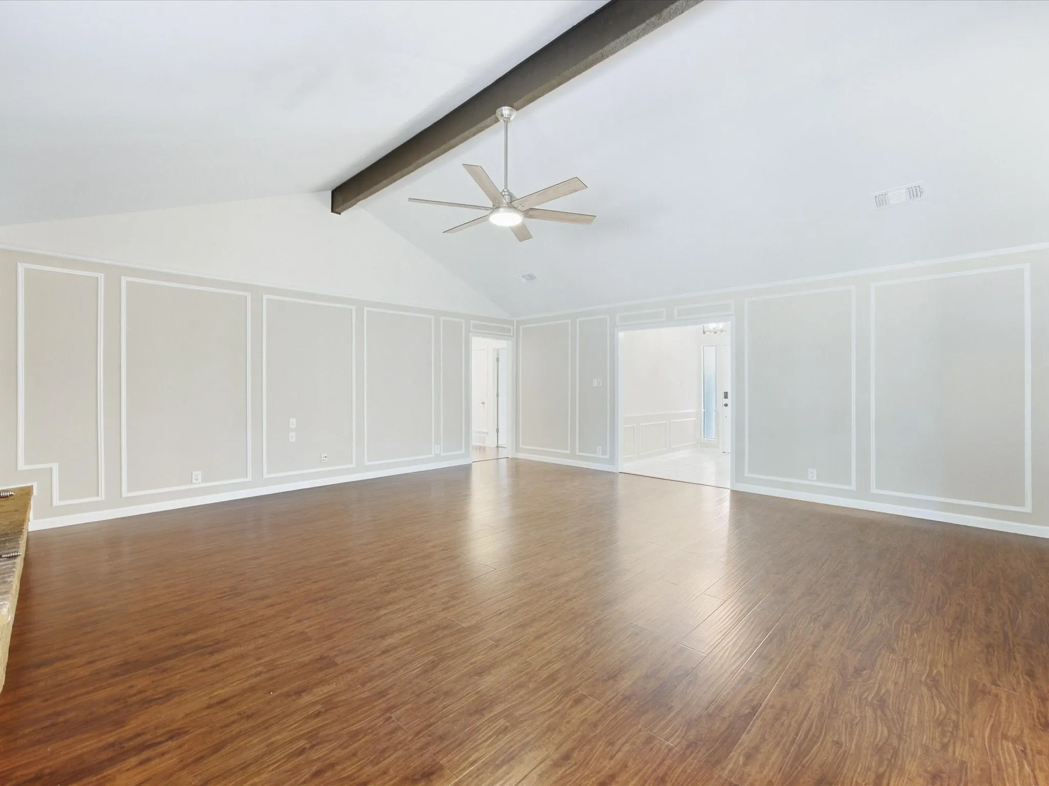 Vaulted ceiling with exposed beam, wood-finish flooring, decorative wall molding, and a ceiling fan with integrated lighting