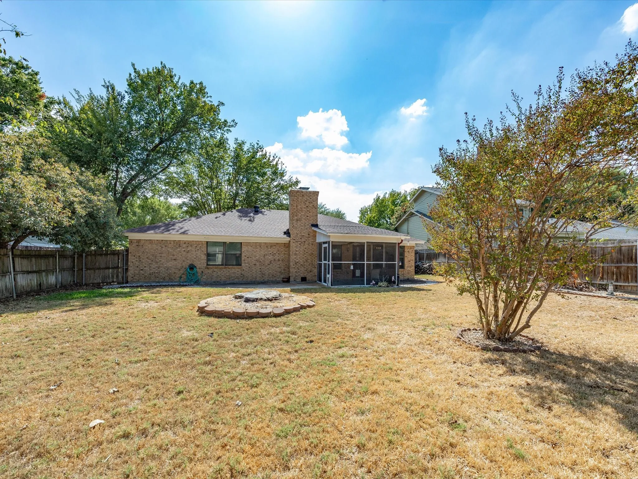 Expansive backyard featuring a brick exterior, screened enclosure, and a stone-lined fire pit