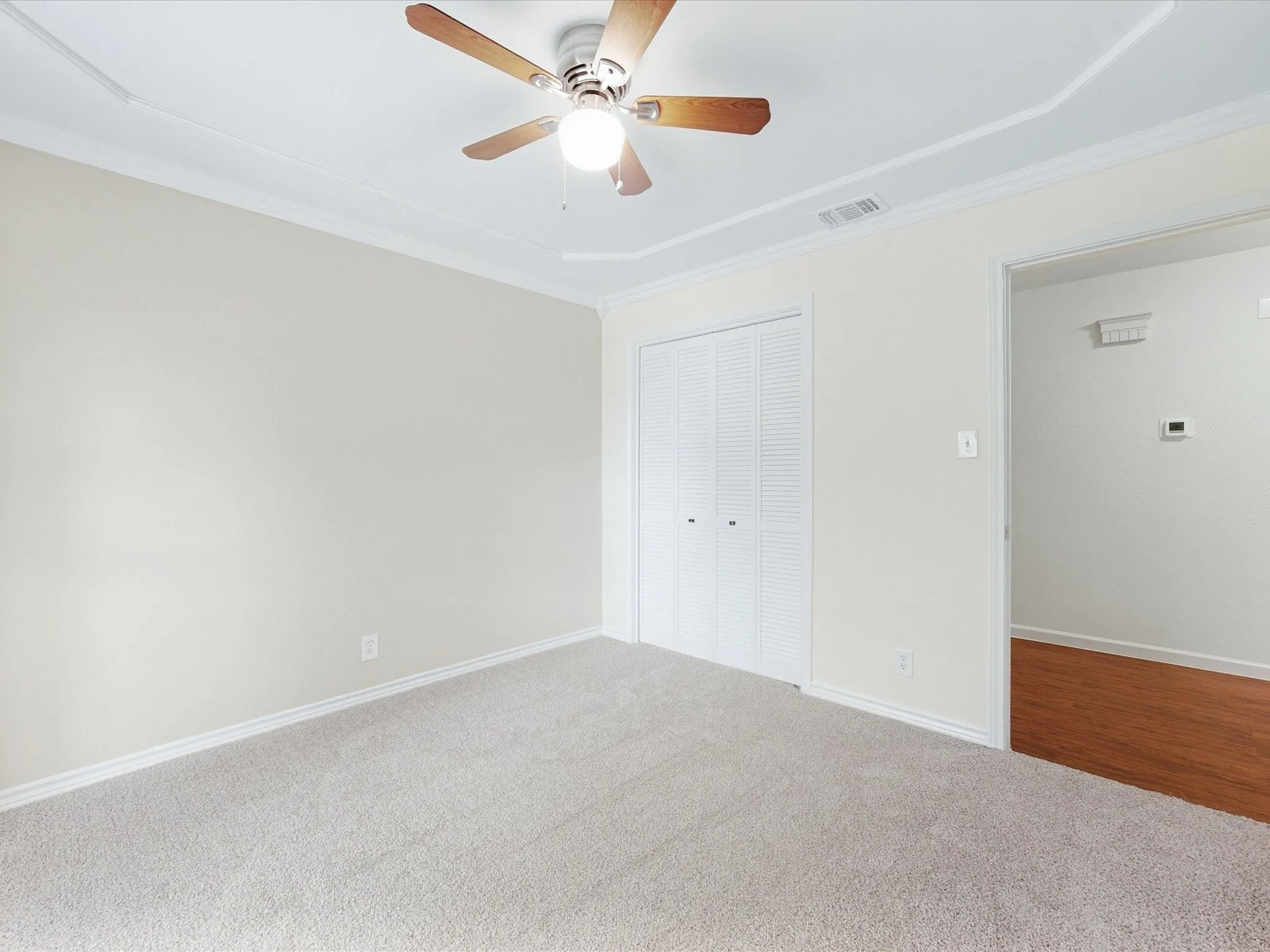 Carpeted room with a ceiling fan, crown molding, and bi-fold closet doors