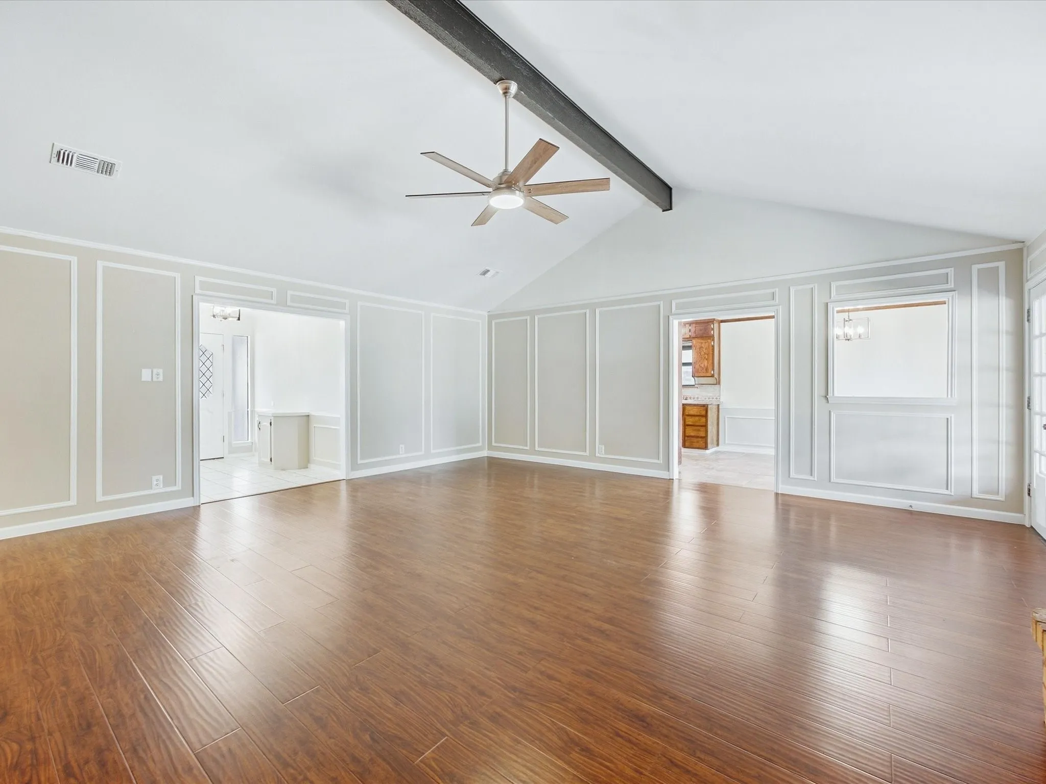 Vaulted ceiling with an exposed beam, wood-finish flooring, and decorative wall molding