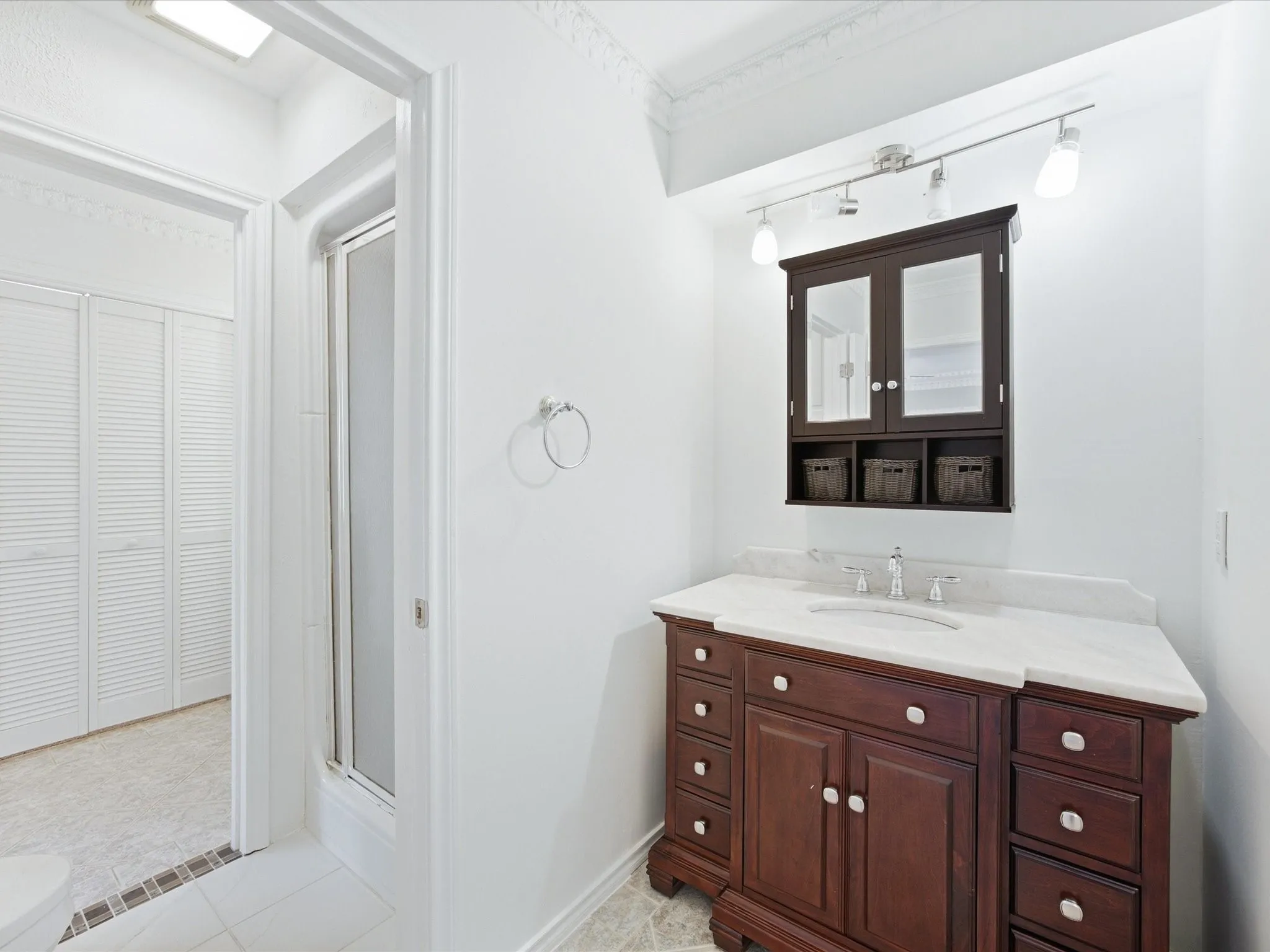 Spa-inspired ensuite bathroom featuring a rich wood-finish vanity with dual sinks, white quartz countertop, polished chrome fixtures, and an illuminated medicine cabinet with mirrored doors