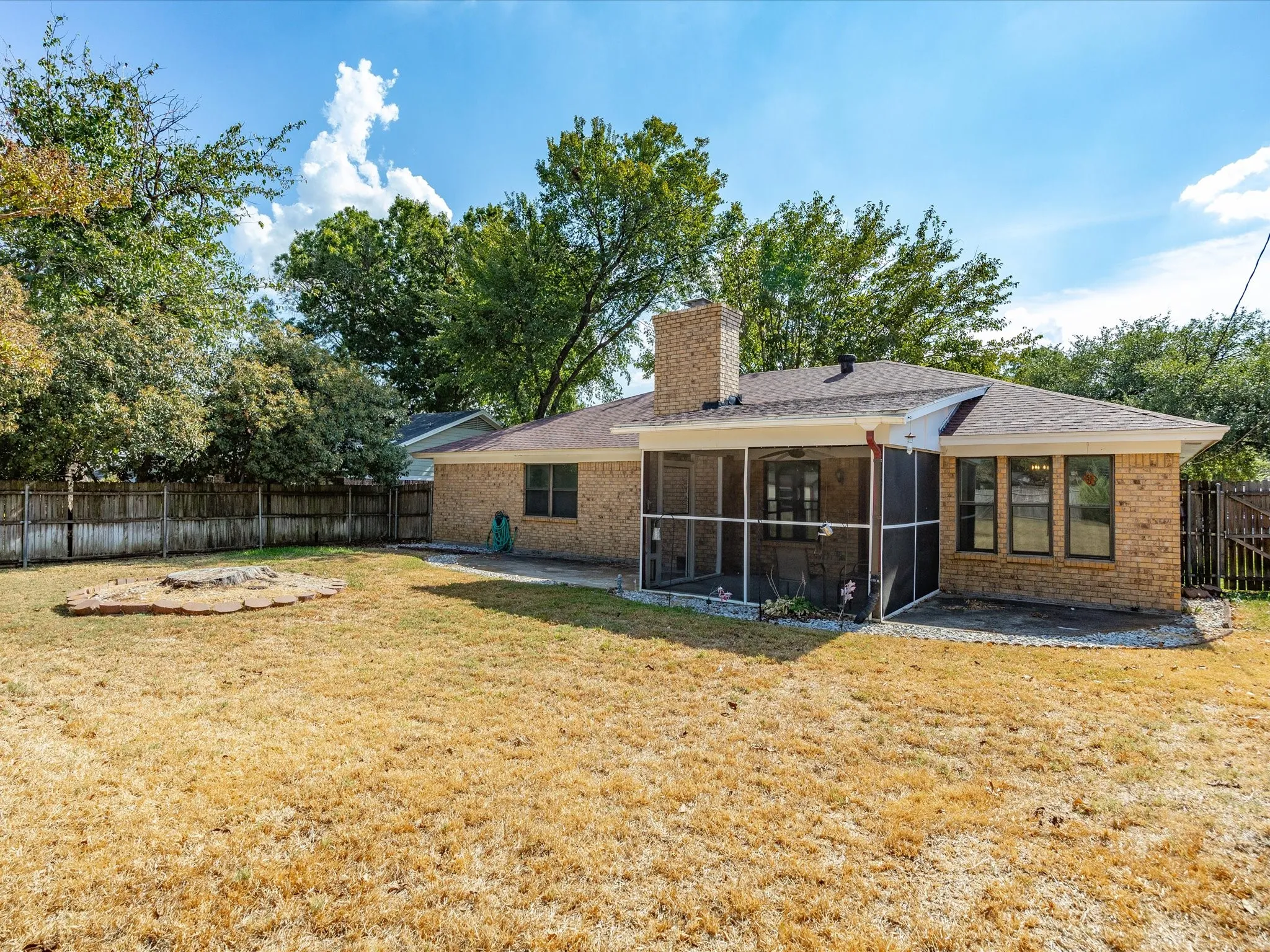 Brick exterior with a screened-in porch, multiple windows, and a fenced yard