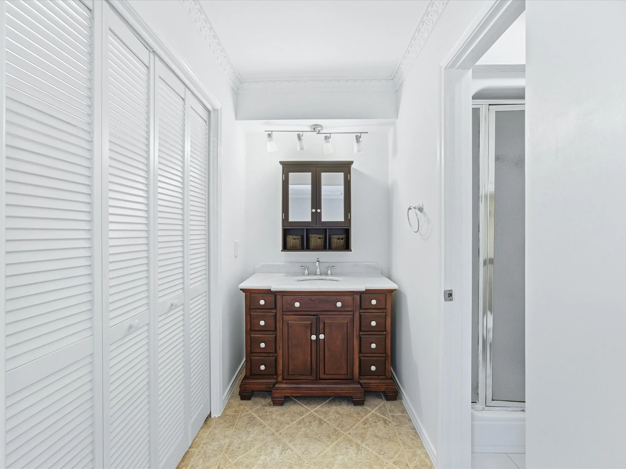 Rich wood-finish vanity with countertop sink, wall-mounted medicine cabinet, and track lighting
