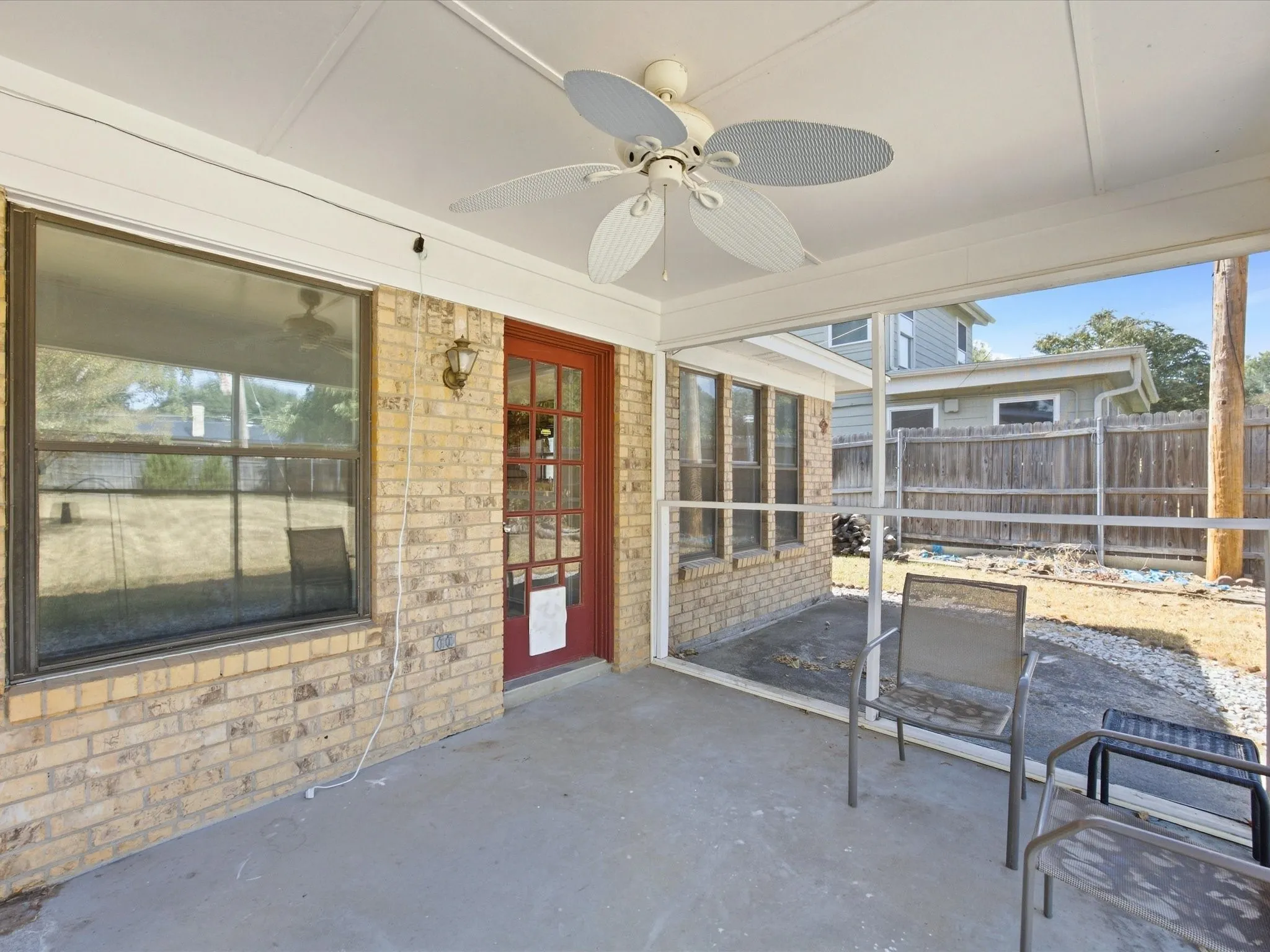 Screened porch with concrete flooring and a ceiling fan, featuring a brick exterior wall with a red glass-paned door