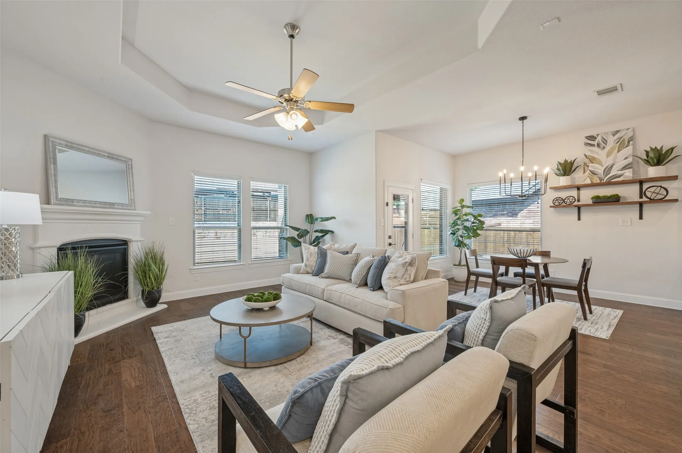Tray ceiling, wood-finish flooring, fireplace with mantel, ceiling fan, and built-in shelving