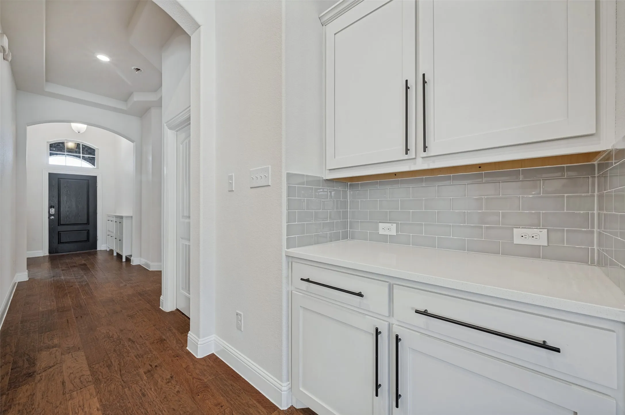 White shaker-style cabinetry with matte black hardware, light-toned countertop, and light gray subway tile backsplash