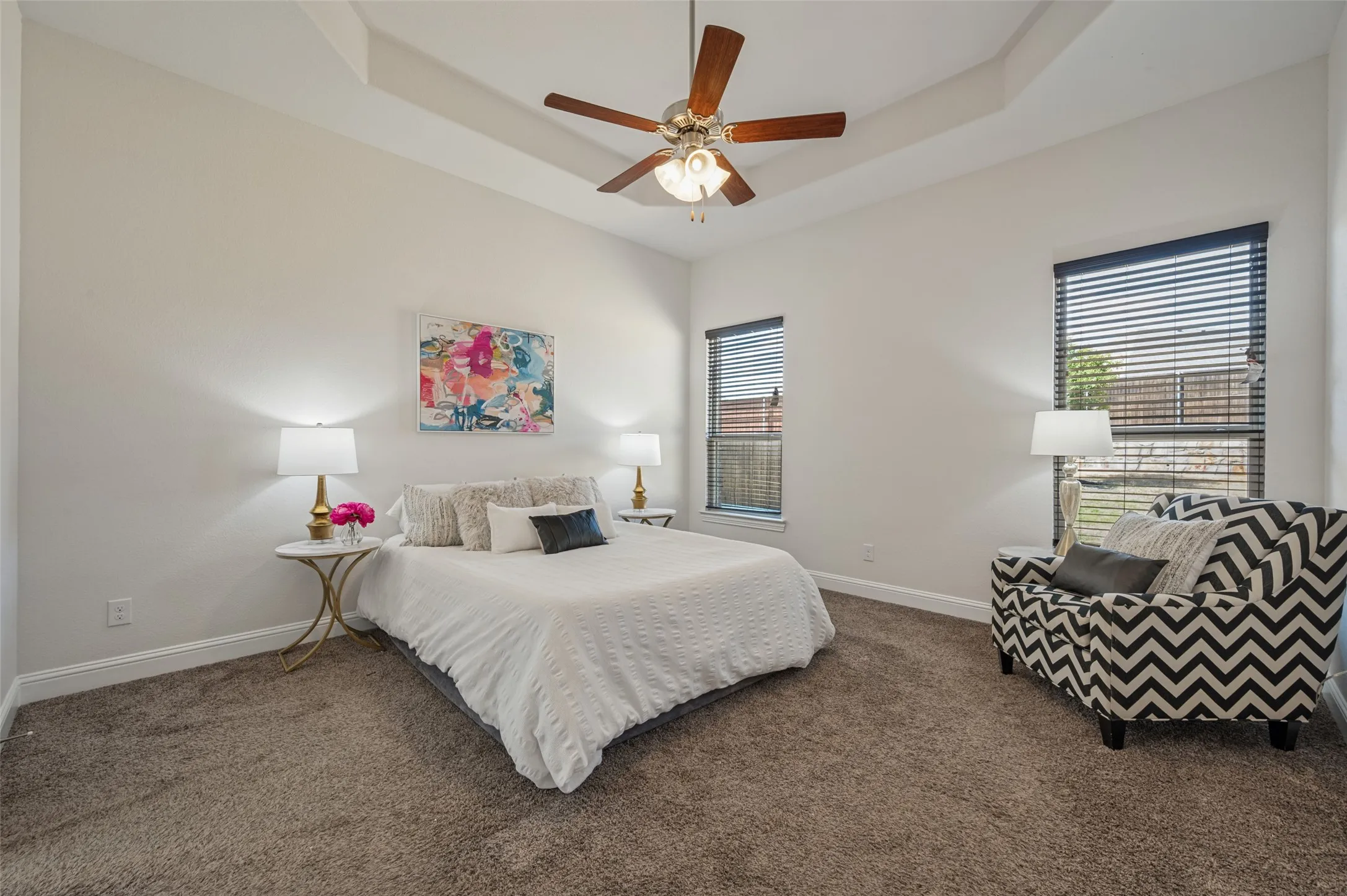 Tray ceiling featuring a ceiling fan, two windows with blinds, and carpeted flooring
