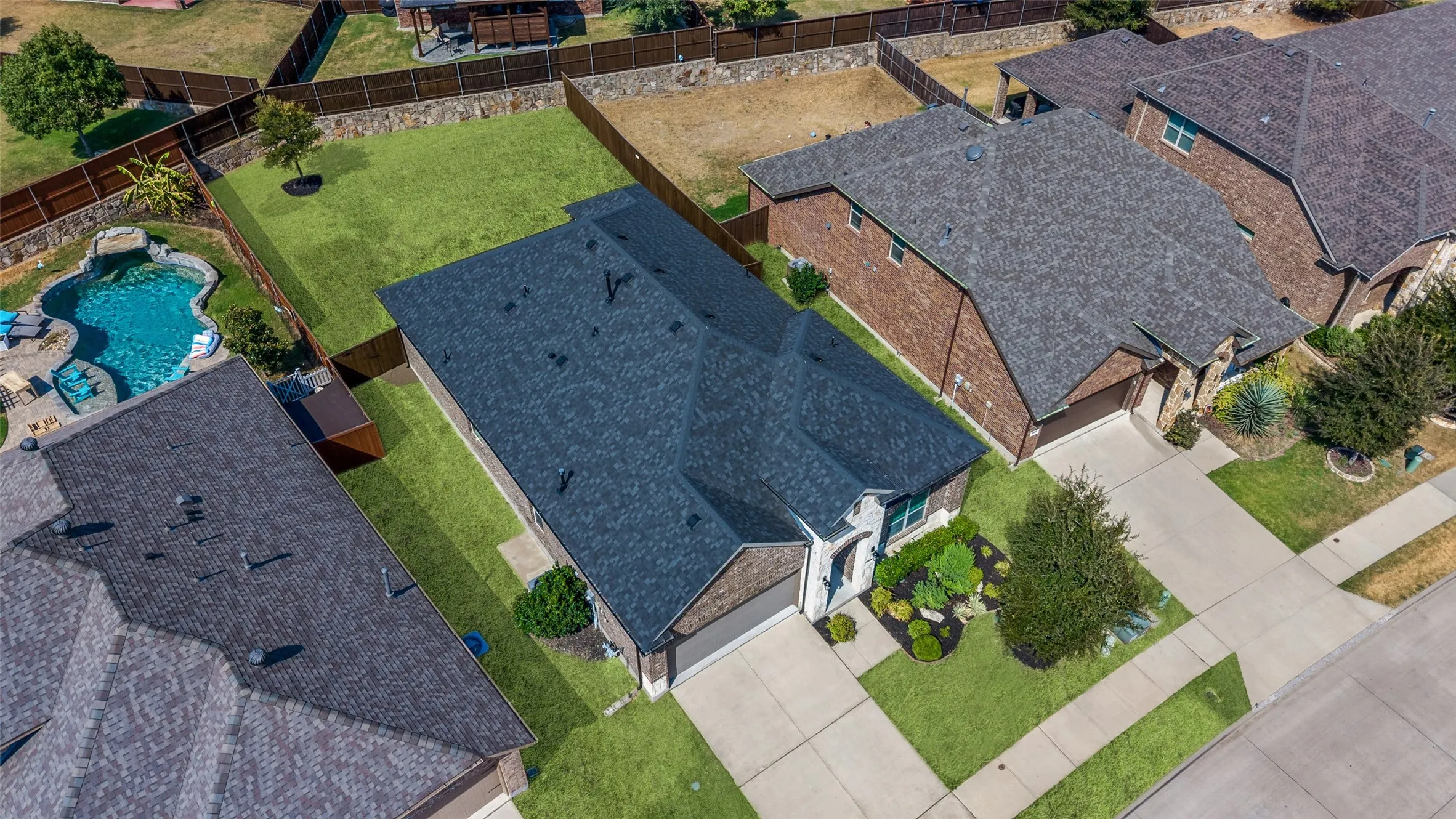 Exterior brick and stone facade, attached two-car garage, established front landscaping, fenced backyard, and paved driveway