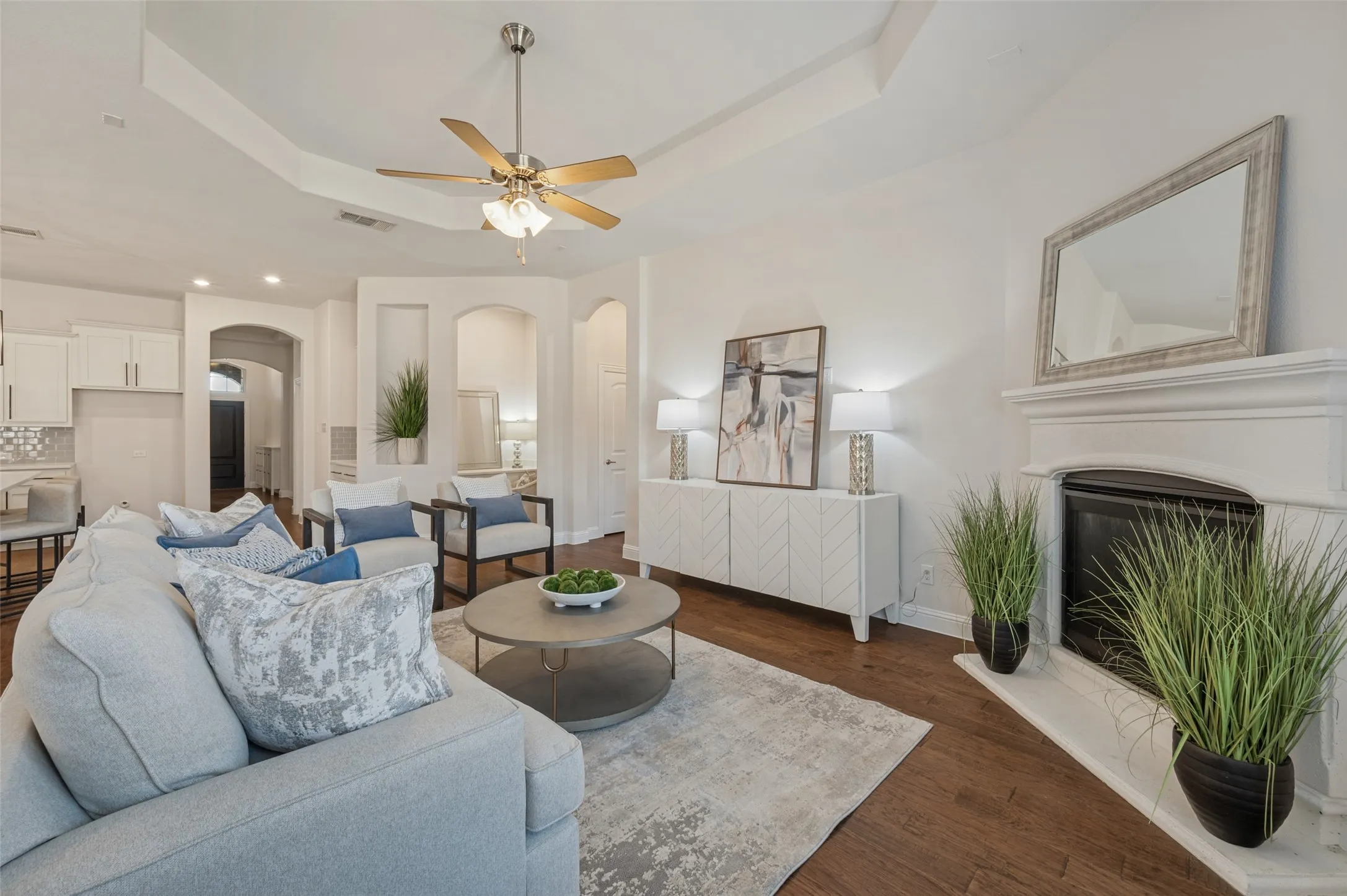 Living area with tray ceiling, wood-finish flooring, recessed lighting, and a built-in fireplace with a white mantel
