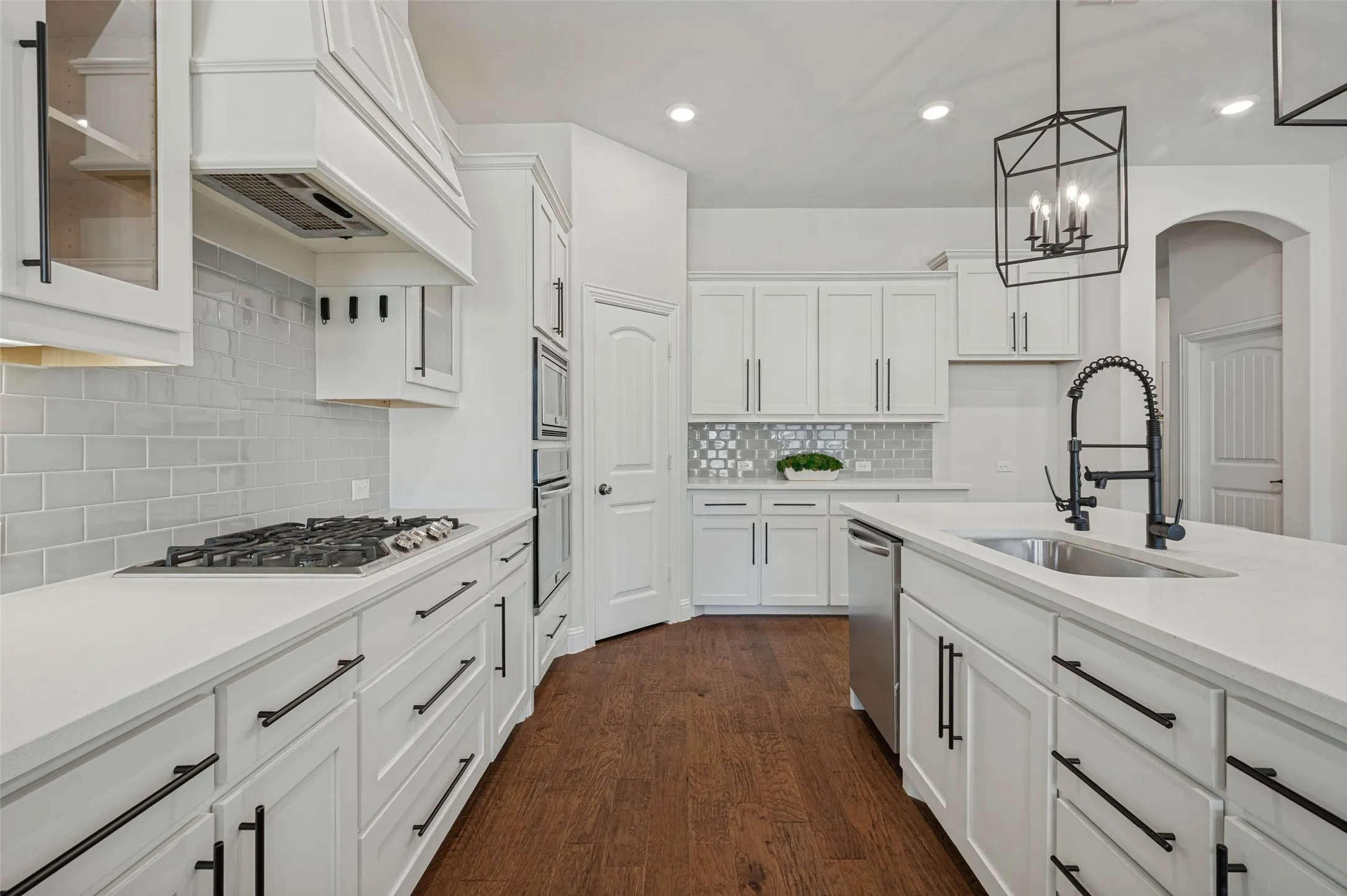 White shaker cabinetry with black hardware, stone countertops, stainless steel appliances, a gas cooktop, and wood-finish flooring