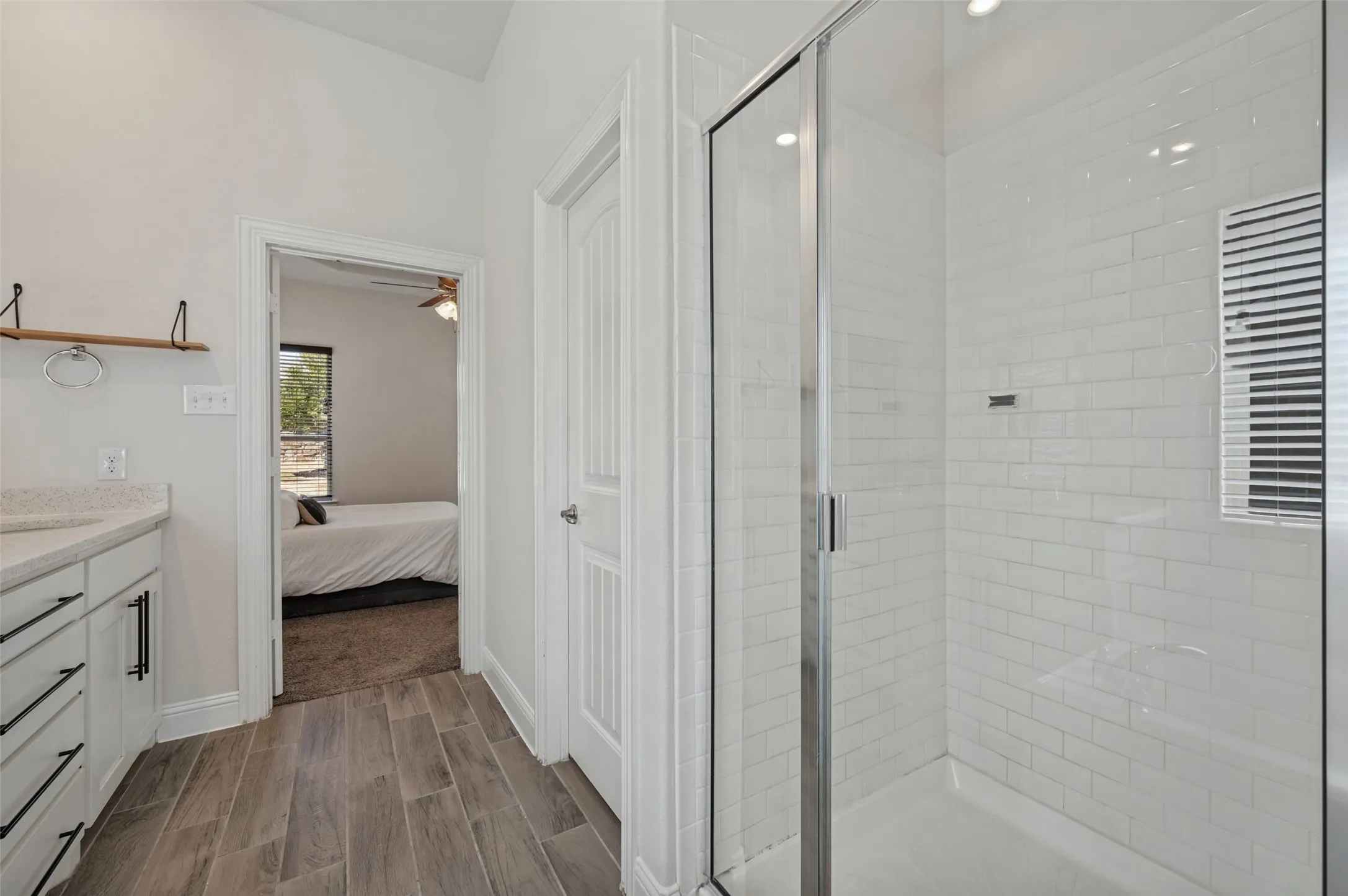 Spacious bathroom featuring wood-look tile flooring, a shower with subway tile surround, and a vanity with a light-toned countertop