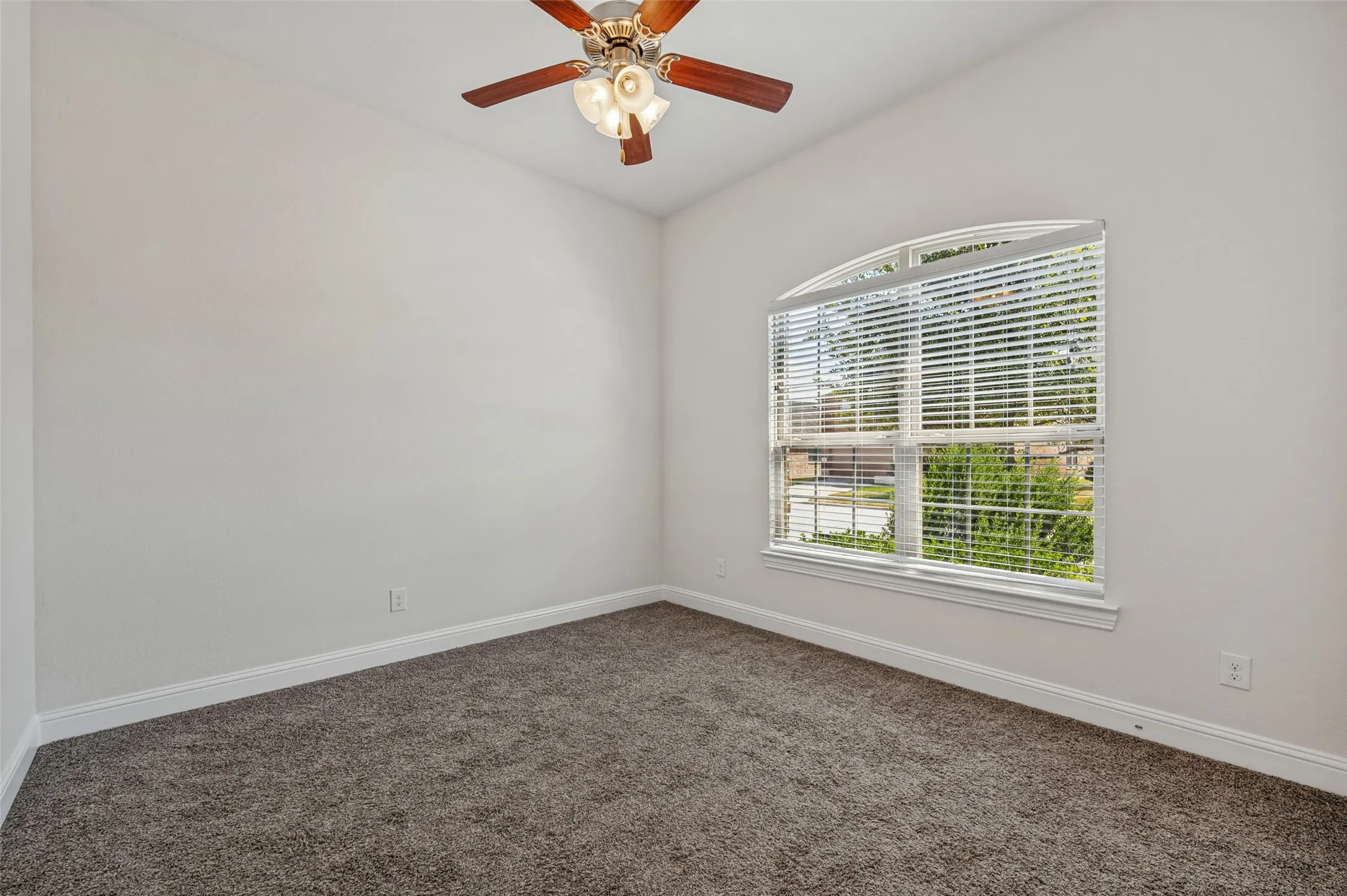 Vaulted ceiling with a wood-finish ceiling fan, arched window with horizontal blinds, and carpeting