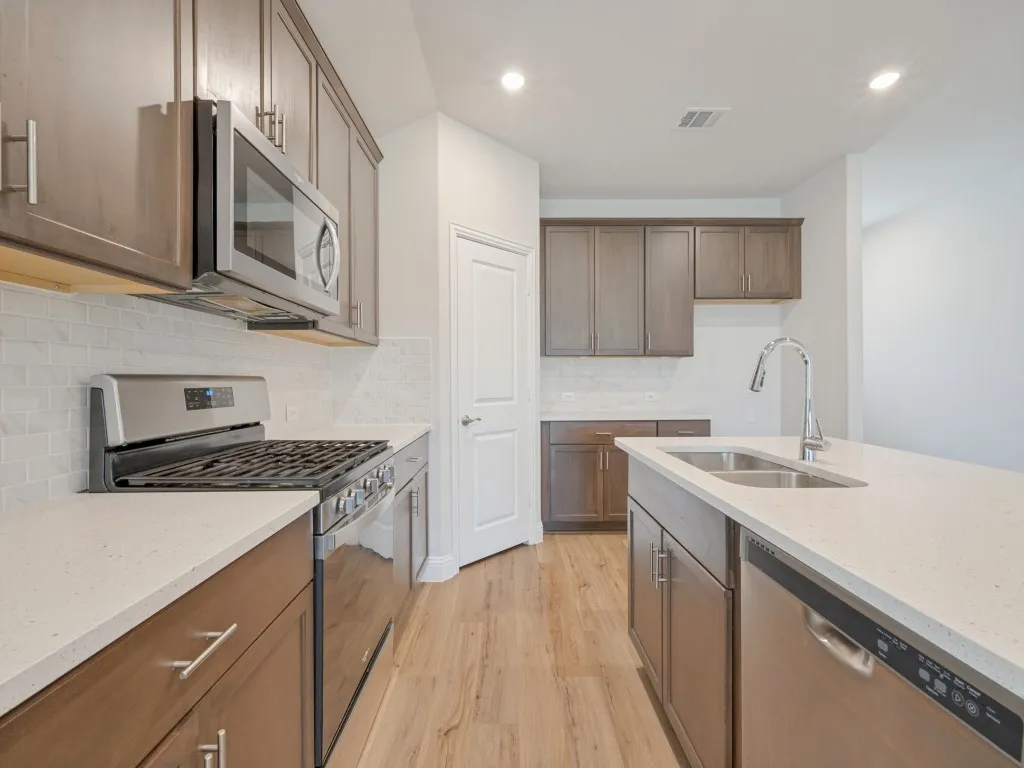 Kitchen featuring wood-finish flooring, stainless steel appliances, white subway tile backsplash, light-toned countertops, and recessed lighting