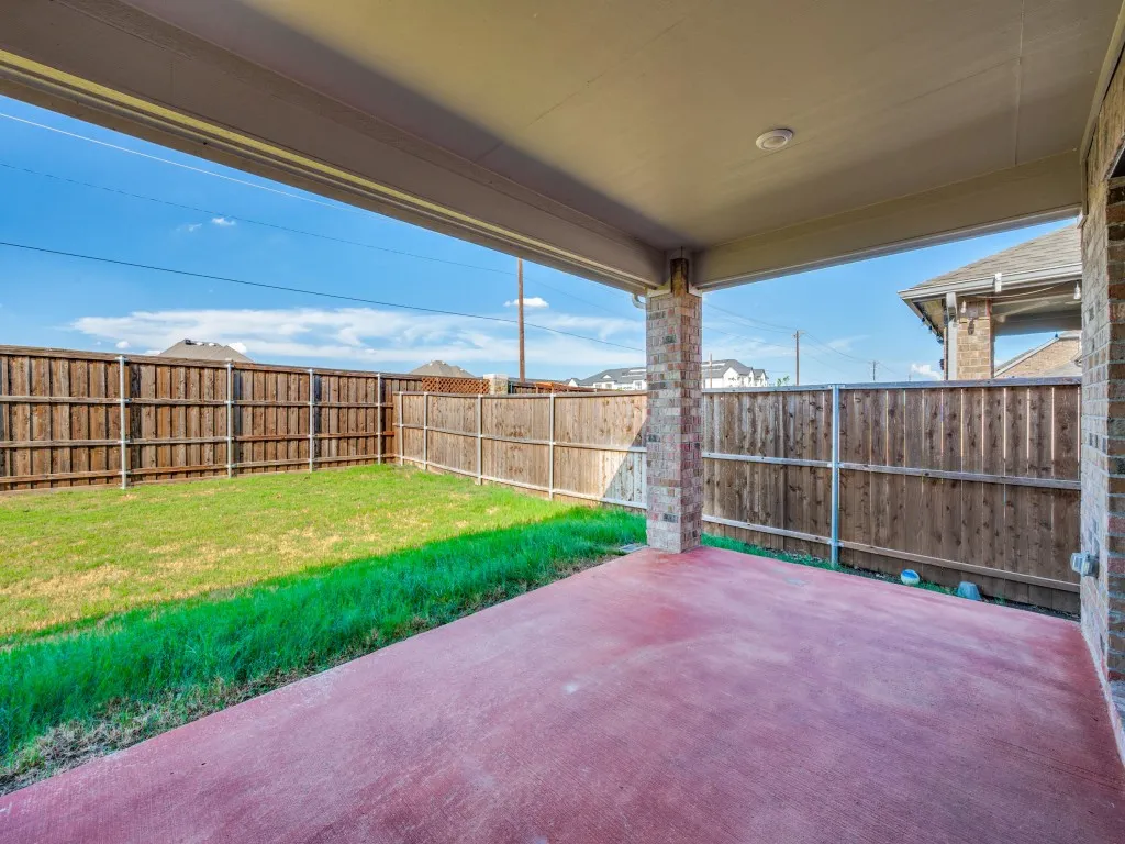Covered patio with brick columns, concrete flooring, and an expansive lawn, enclosed by a wood privacy fence