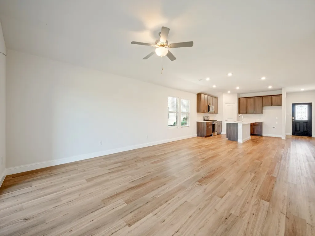 Open-concept layout featuring wood-finish flooring, recessed lighting, ceiling fan, and a kitchen with wood cabinetry and a central island