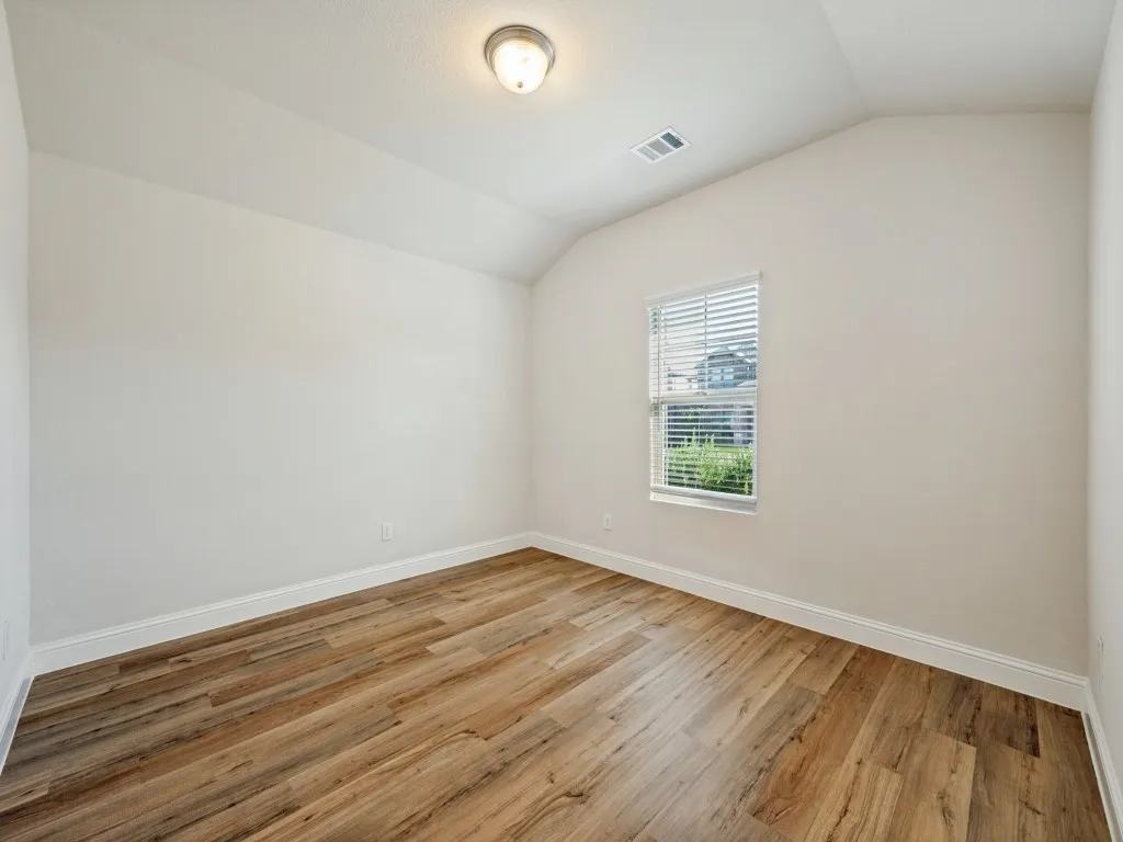 Vaulted ceiling with a flush-mount light fixture, wood-finish flooring, and a single window with blinds